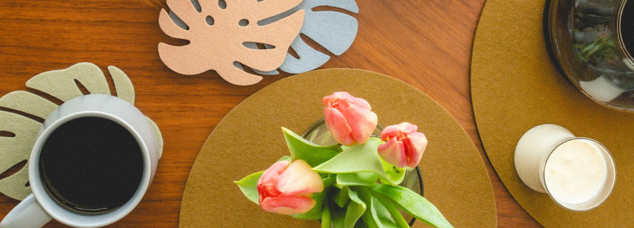 A designer tabletop set on a burl wood table with four place settings, red and white accents, napkins, plates, and drinkware. Text: The Designers Table Edit and product notes.