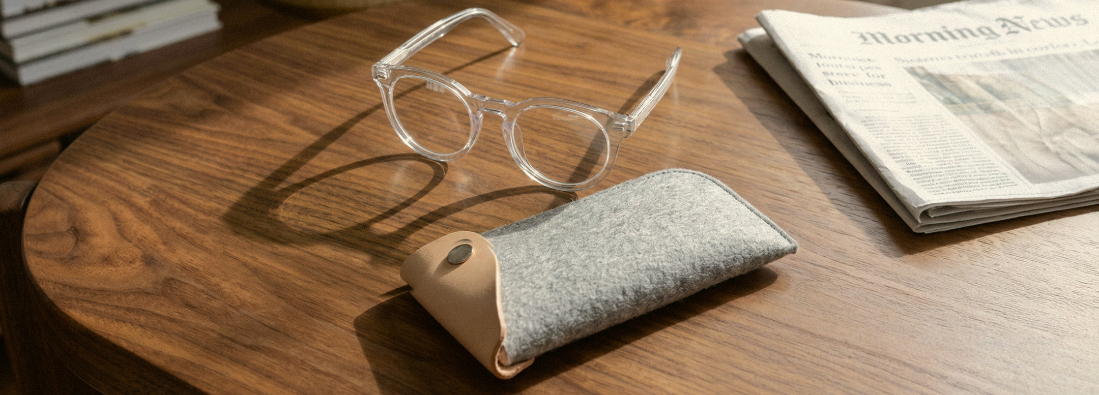 Two green felt eyeglass cases with brown leather trim sit on a wooden surface. One case is open, revealing a pair of glasses inside.