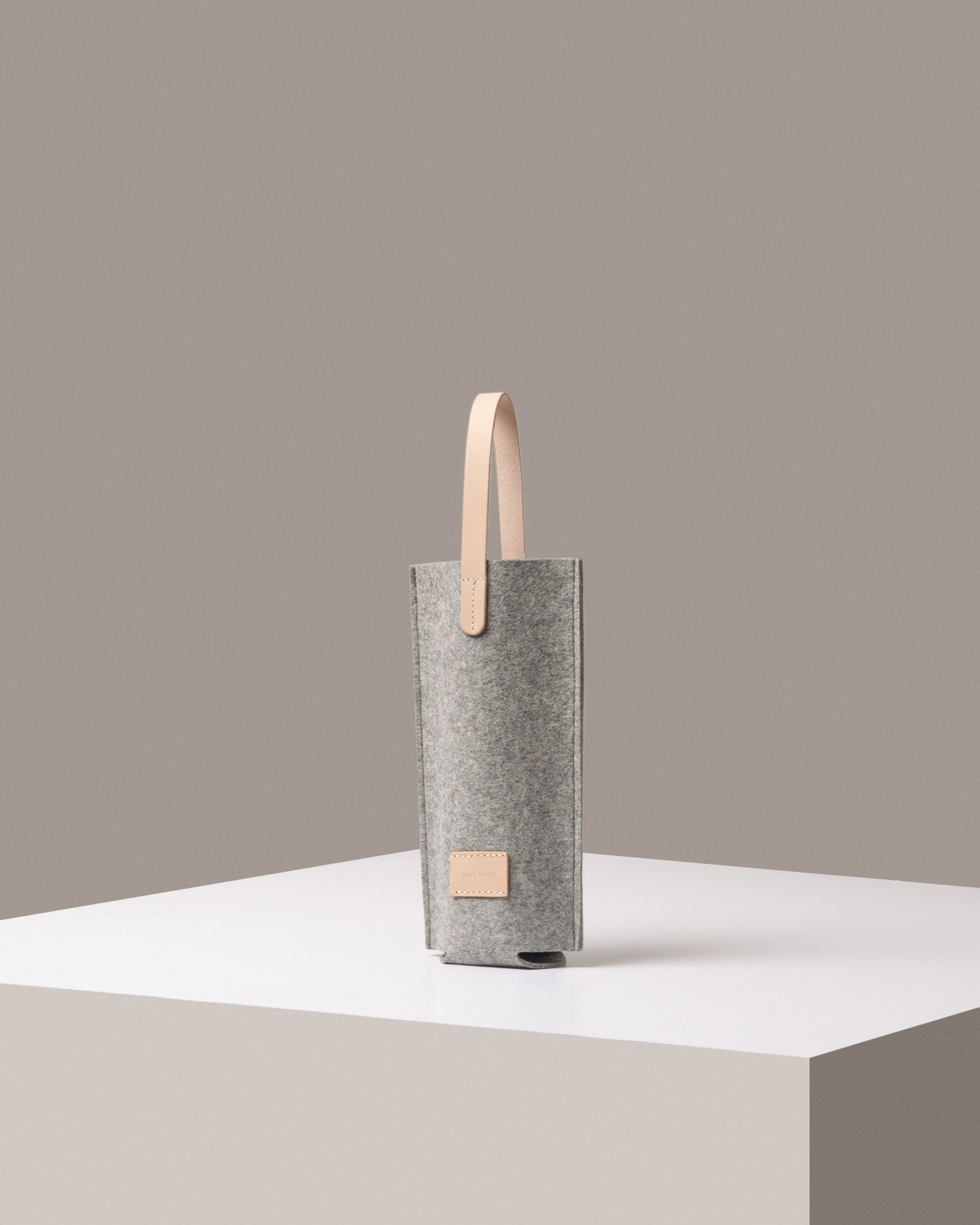 A stylish Hana Merino Wool Bottle Bag in light gray, displayed in a three-quarter view on a white base