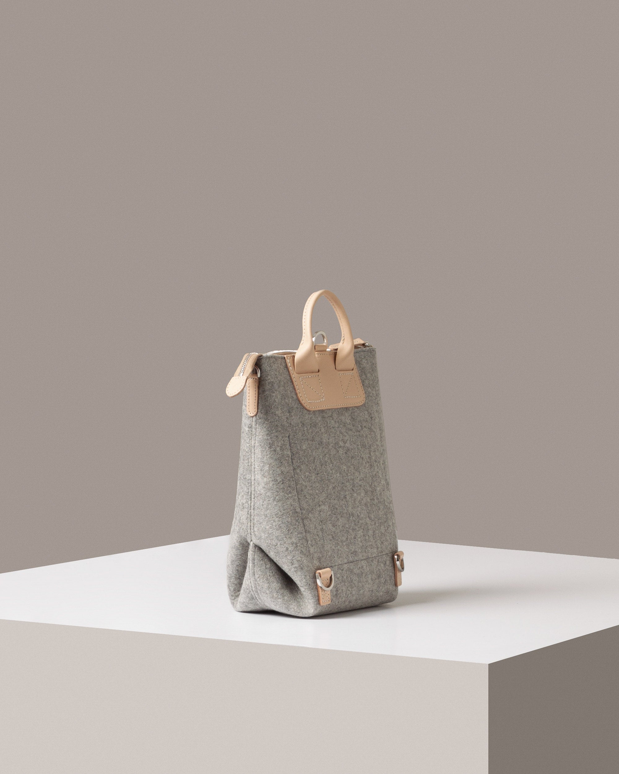 A light grey Bedford Merino Wool Felt Midi Backpack on a white base displayed in a side-view