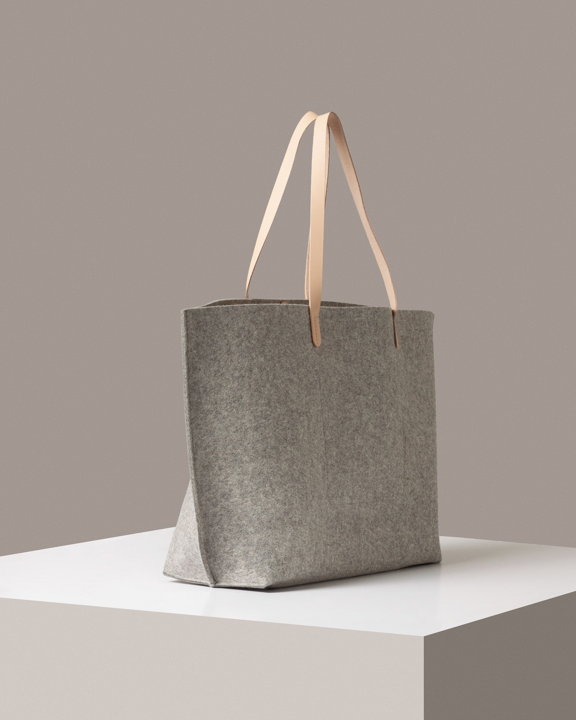 A Hana Merino Wool Felt Boat Bag in gray and beige colors on a white base displayed in a side-view