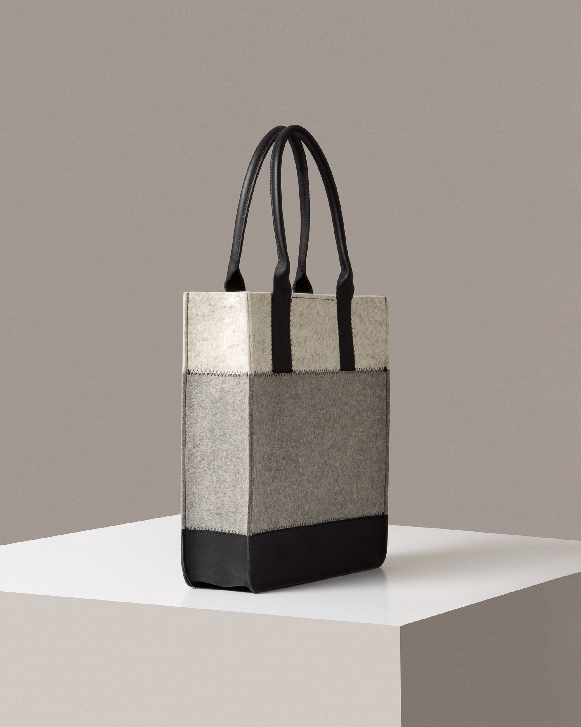 A Jaunt Merino Wool Felt Tote in gray, white, and black colors on a white base displayed in a side-view