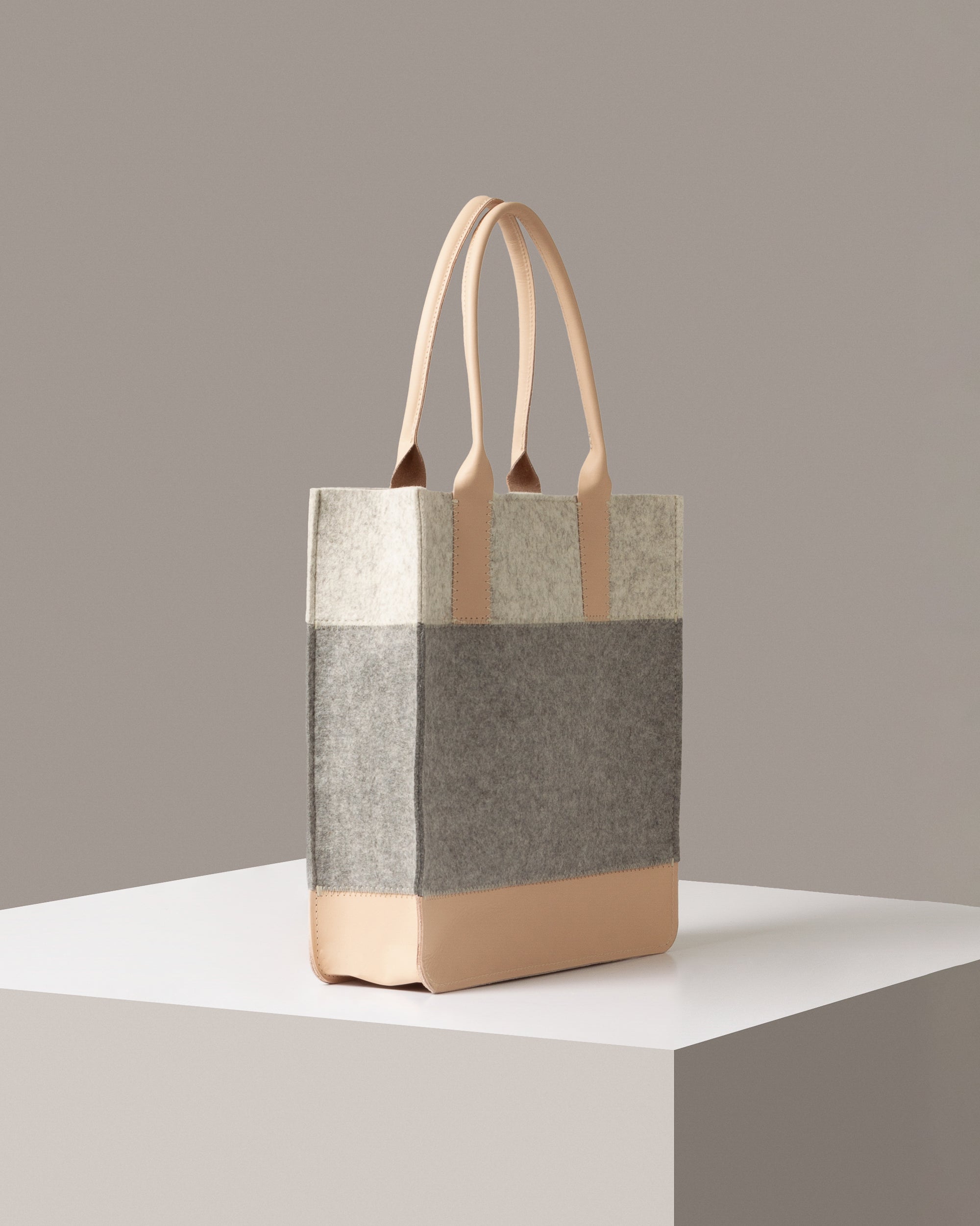 A Jaunt Merino Wool Felt Tote in white, gray, and beige colors on a white base displayed in a side-view
