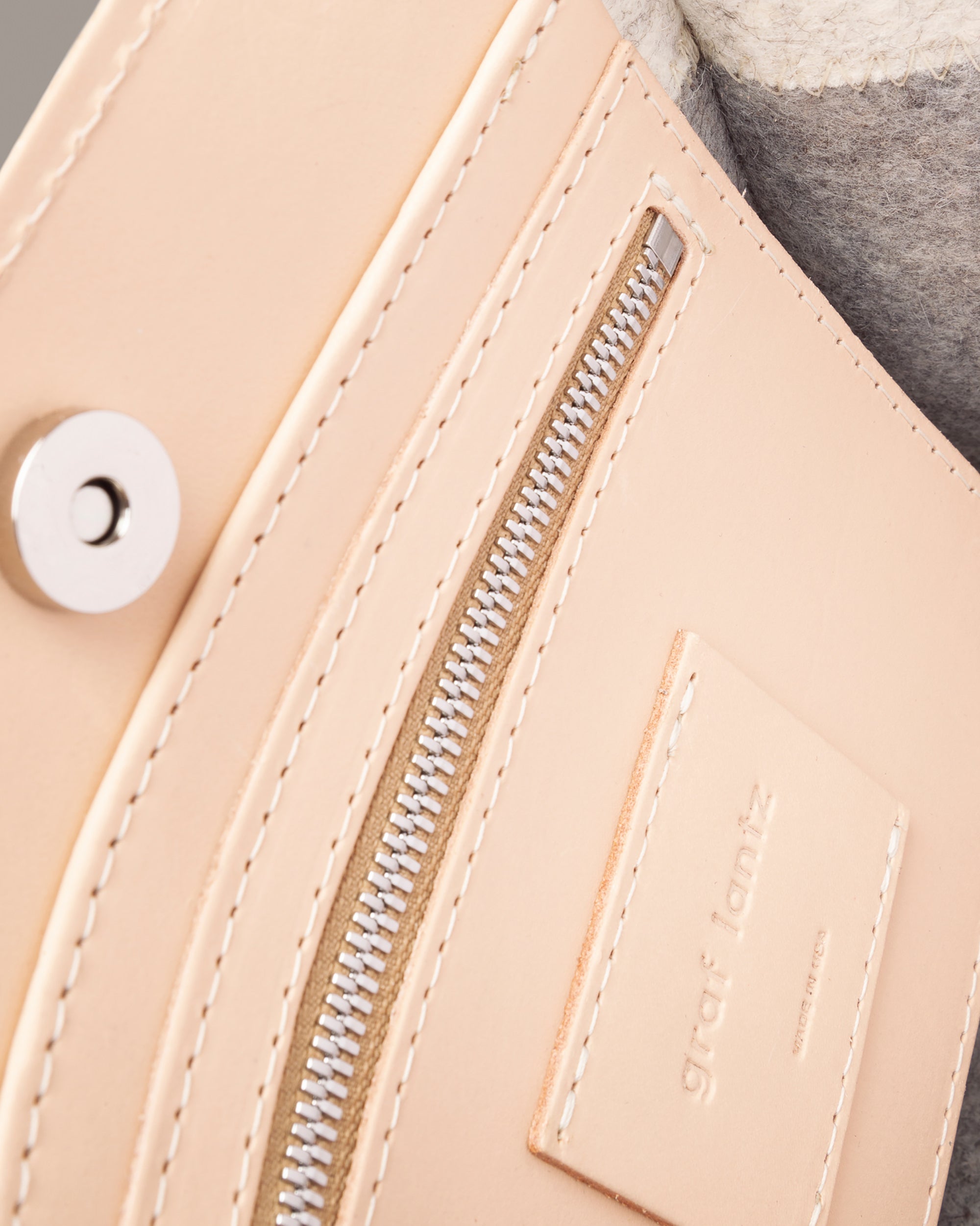 Interior view of a gray Jaunt Mini Merino Wool Felt crossbody bag featuring a zippered-leather pocket, beige leather trim, and a magnetic snap closure, highlighted in detail
