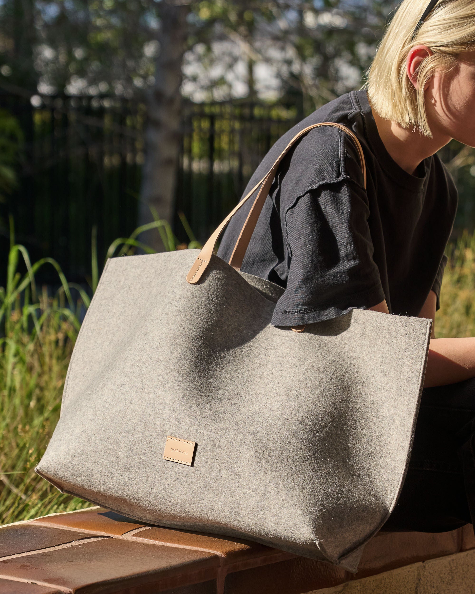 Woman sitting outdoors with a grey Hana Merino Wool Felt Boat Bag on her side, highlighting casual elegance