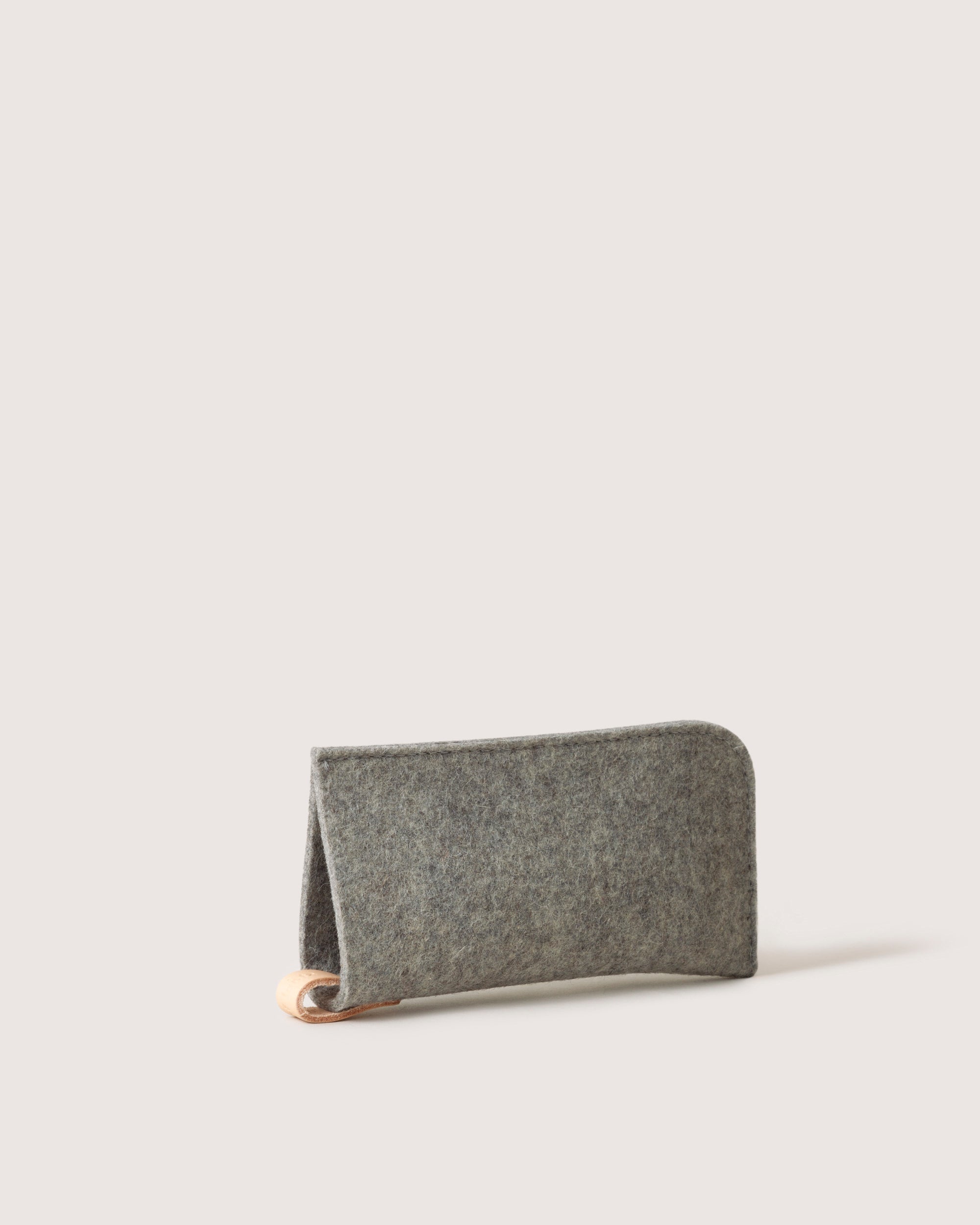 The graf lantz minimalist grey felt wallet, made from Merino wool with a tan leather corner accent, stands upright against a plain light background. Its design is simple and modern.