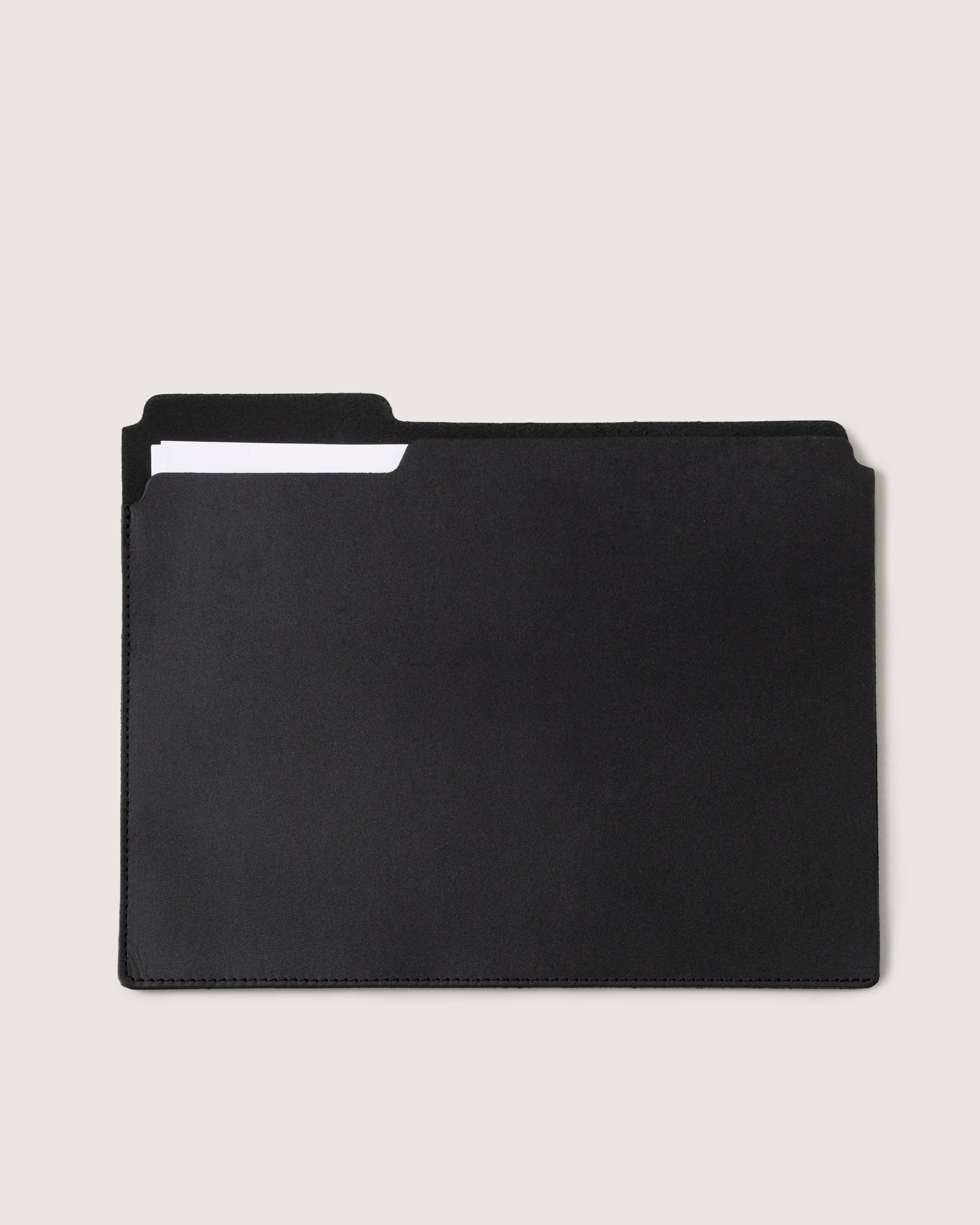 The graf lantz black leather file folder, crafted from vegetable-tanned leather, is showcased against a light background. The minimalistic design reveals the edge of a letter-sized paper and a partially visible white tab inside.