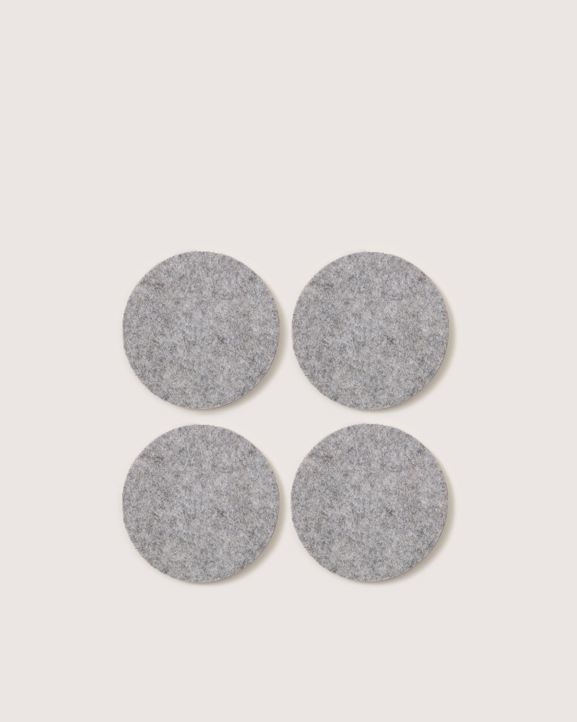 The graf lantz set includes four round, gray felt pads made from soft German Merino wool. These pads add elegance and protect surfaces from scratches, arranged in a square formation on a white background.