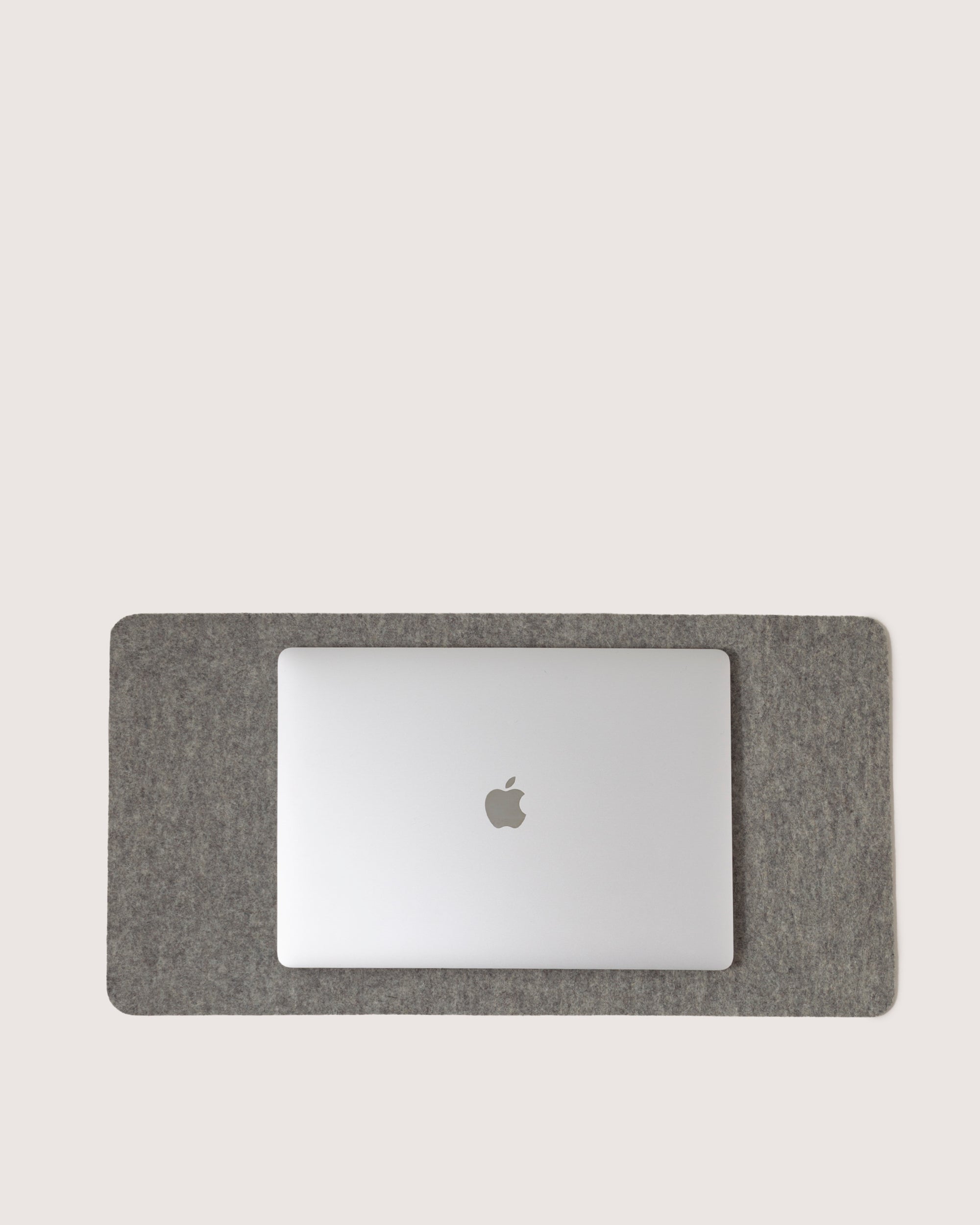 A silver laptop with a recognizable logo sits on a rectangular gray graf lantz Mosen Desk Pad against a light background, enhancing any workspace with stylish practicality for both professionals and students.