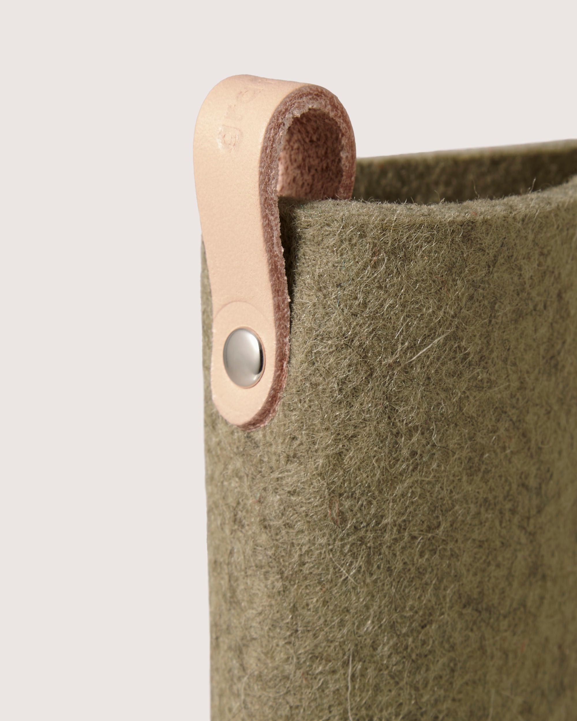 A close-up of a graf lantz green felt bag made from Merino wool, featuring a beige leather strap loop secured with a metal rivet. Crafted for eyewear protection, it has a textured surface with the strap attached at the top corner against an off-white background.