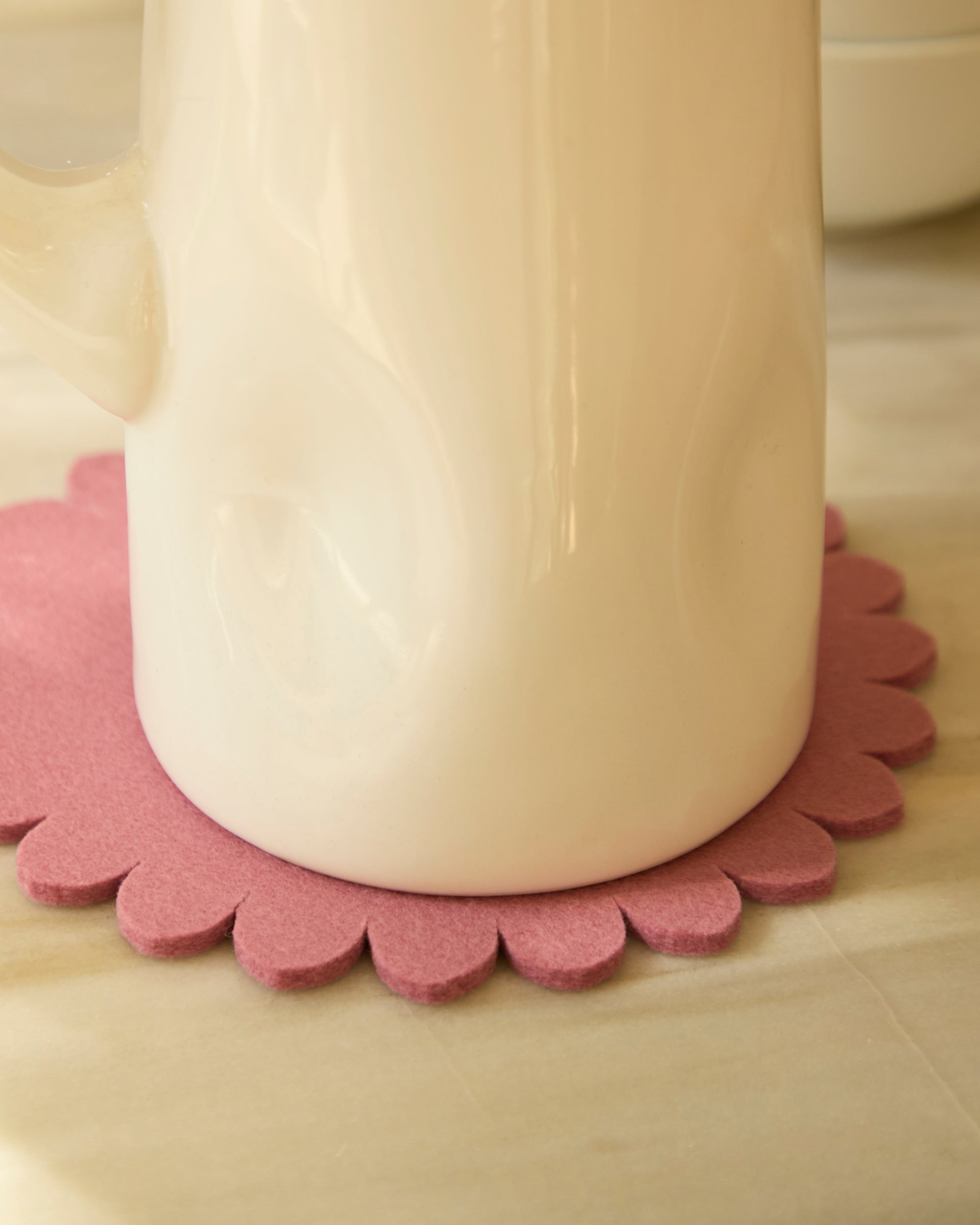 White mug on a Mauve pink floral trivet on a wooden surface