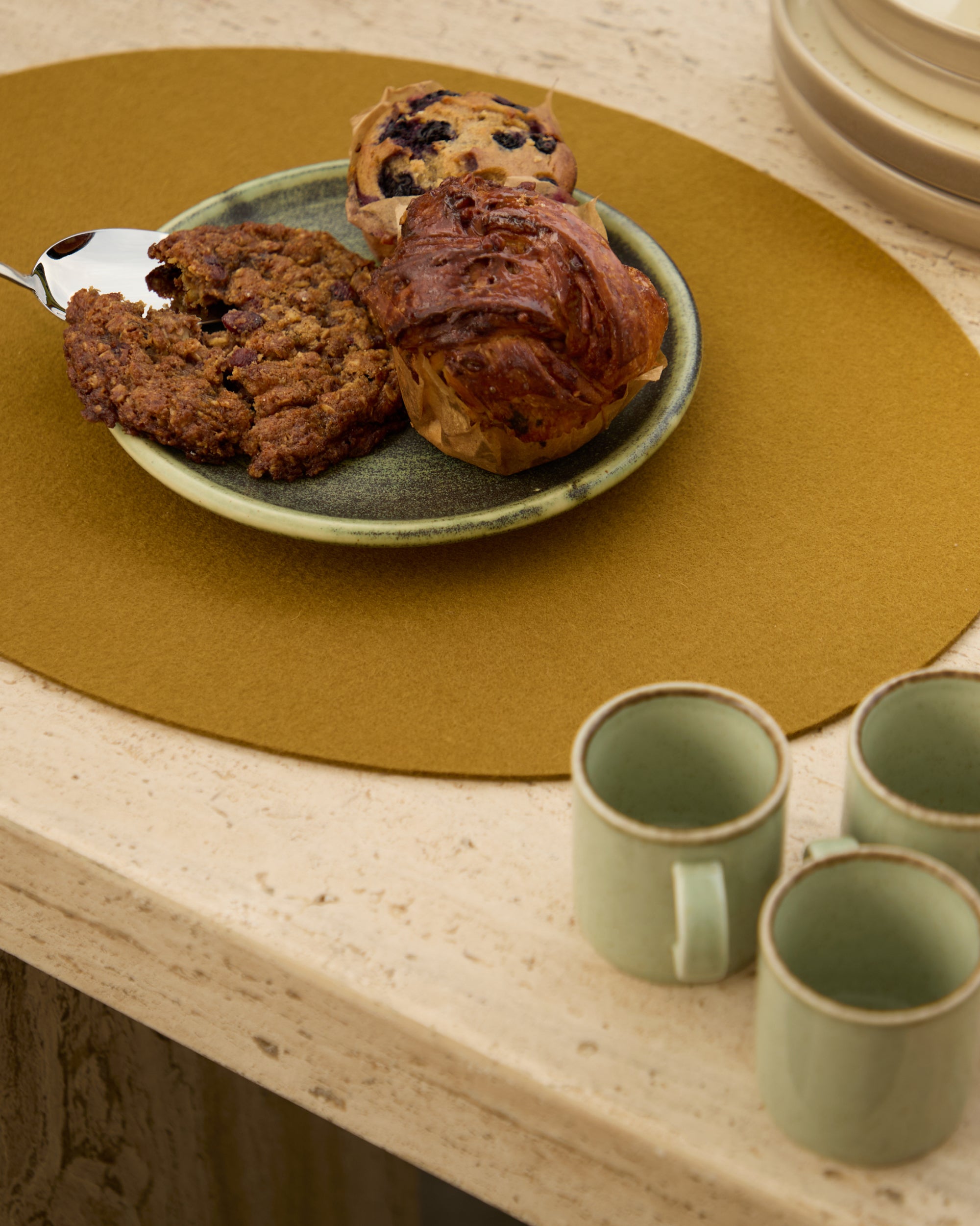 Plate of muffins on a wooden table with green mugs.