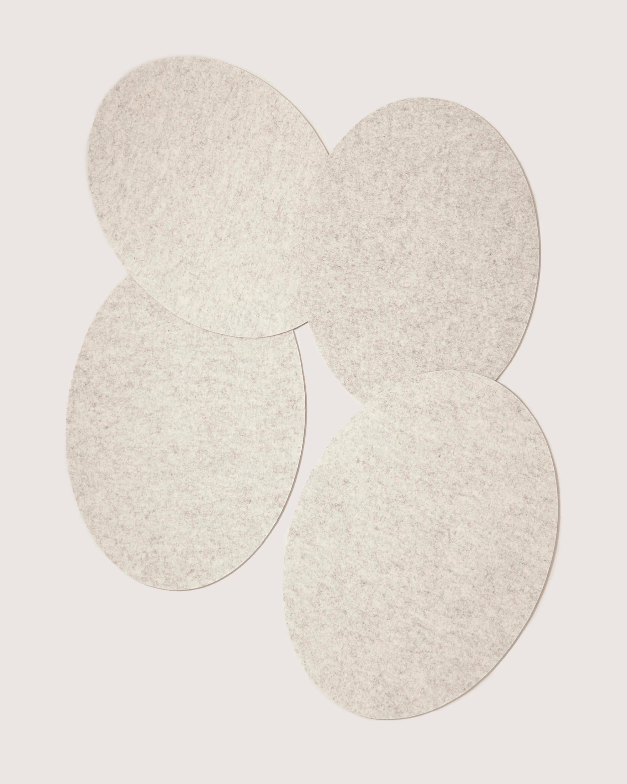 Graf lantz offers sustainable Merino wool felt pads in a light gray, oval design. Arranged artfully on a white background, these designer-inspired pads have overlapping edges that create a unified pattern with a soft texture.