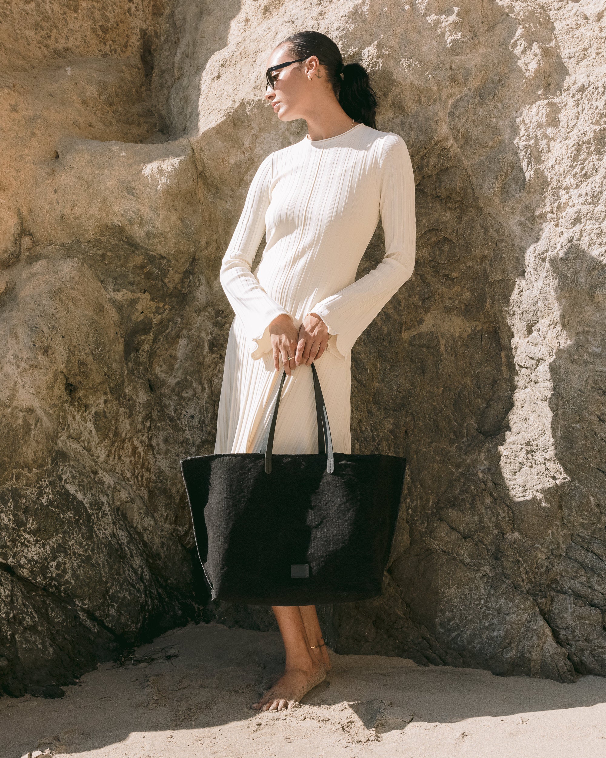 The large Hana Canvas Boat Bag by graf lantz features a simple, black tote design with two thin genuine leather handles and a small rectangular label on the front. Its design includes pockets for easy organization, all set against a plain white background.