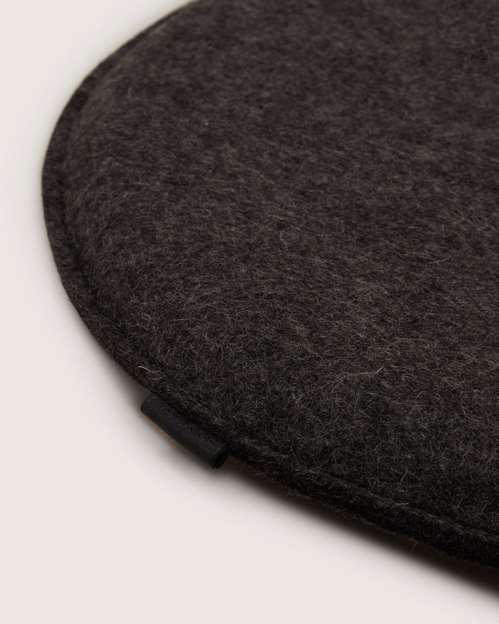 Close-up of a dark gray beret from graf lantz, crafted in soft Merino wool with a subtle texture. It has a rounded, neatly stitched edge and a small loop tab on one side. The plain off-white background enhances its elegant simplicity.