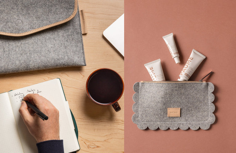 A hand writes in a notebook beside a cup of coffee, a grey felt laptop sleeve, and a scalloped grey pouch holding skincare products, all on a wooden and pink surface.