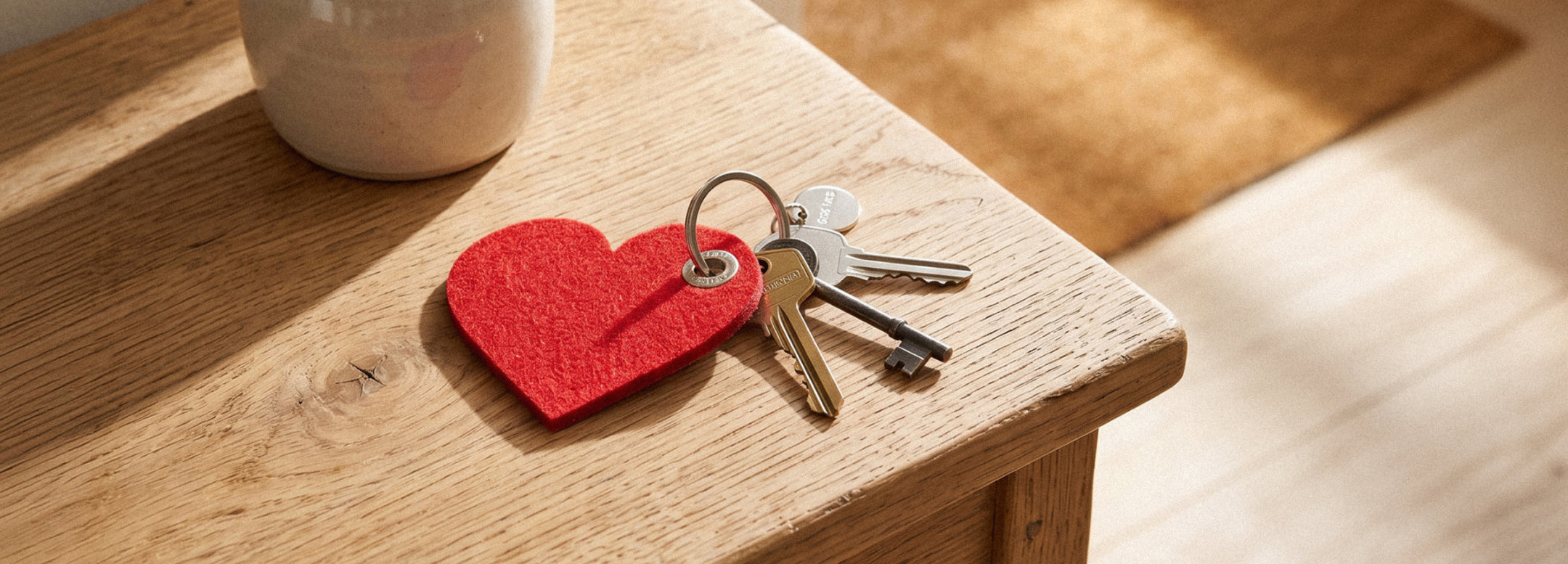 A person in a cream sweater holds a keyring with a house key attached to a red felt heart shape, suggesting the concept of key to my heart.