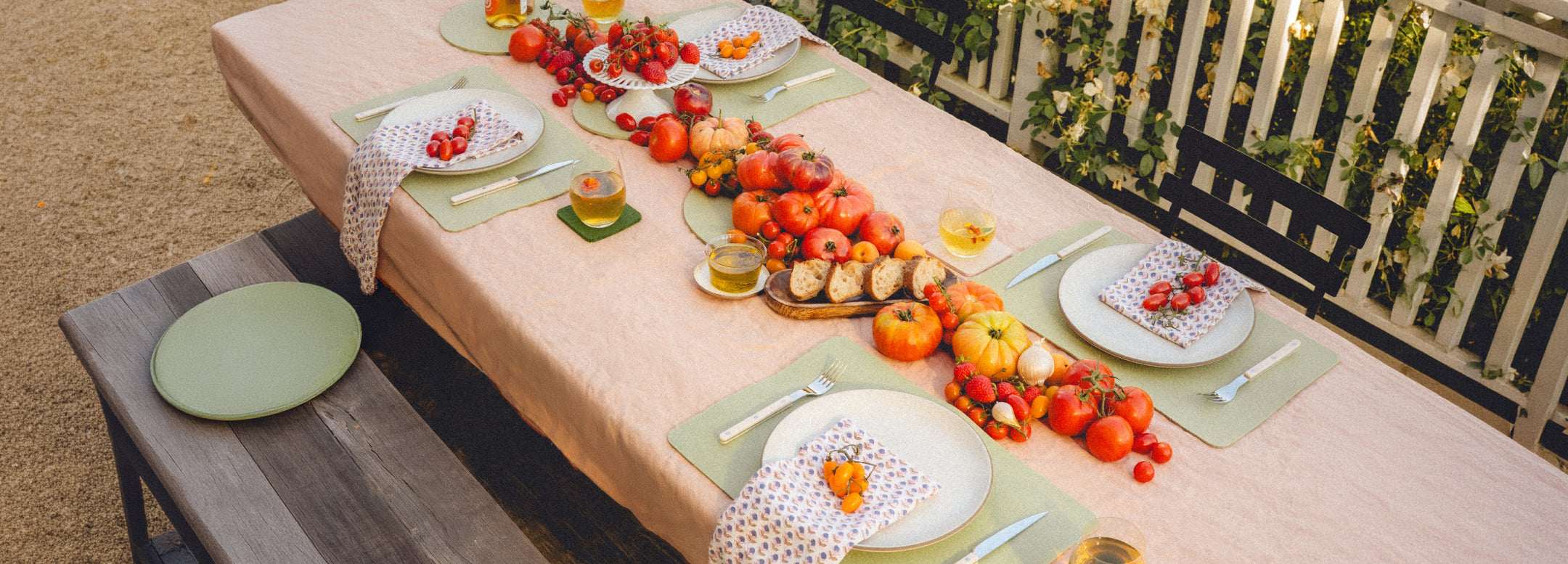 A table with four place settings features various pastries, a bowl of yogurt with fruit, glasses of water, and a persons arm reaching for food. Plates are on brown placemats.