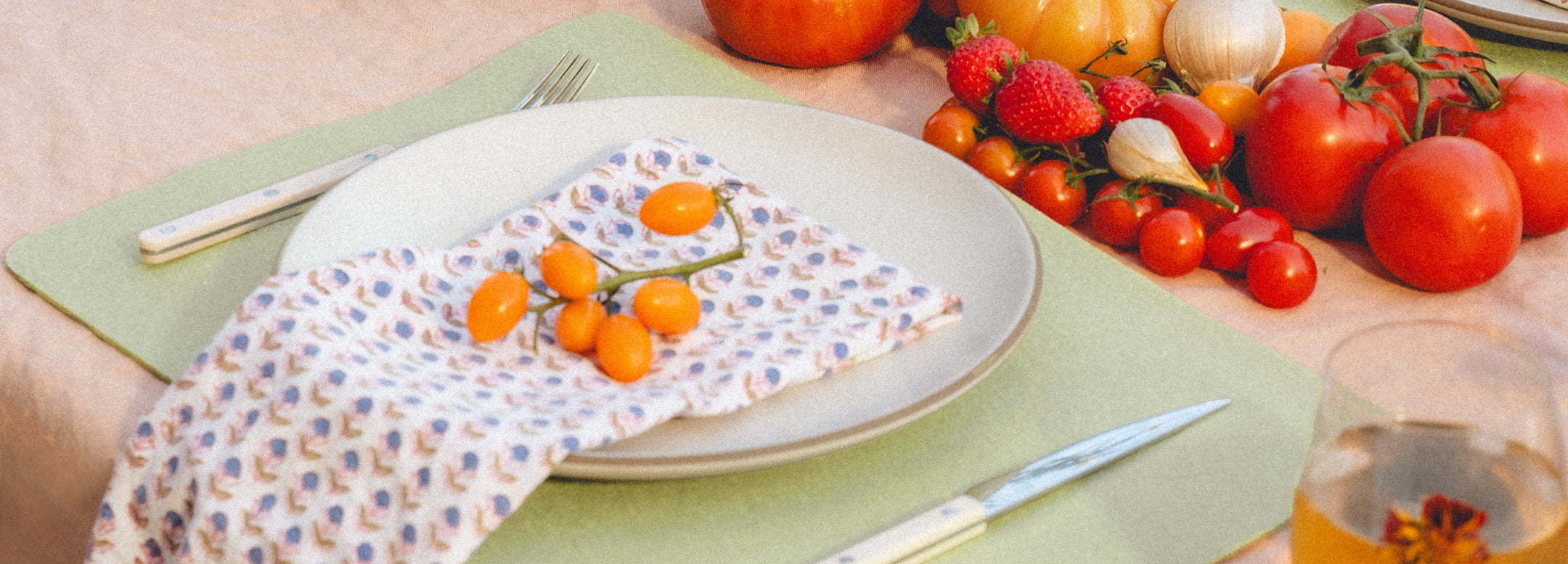 Aerial view of a dining table with navy placemats, white plates, and wine glasses. Hands reach for a charcuterie board and one pours white wine. The setting has neutral tones and elegant tableware.