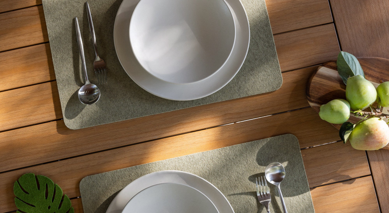 A table with four place settings features various pastries, a bowl of yogurt with fruit, glasses of water, and a persons arm reaching for food. Plates are on brown placemats.