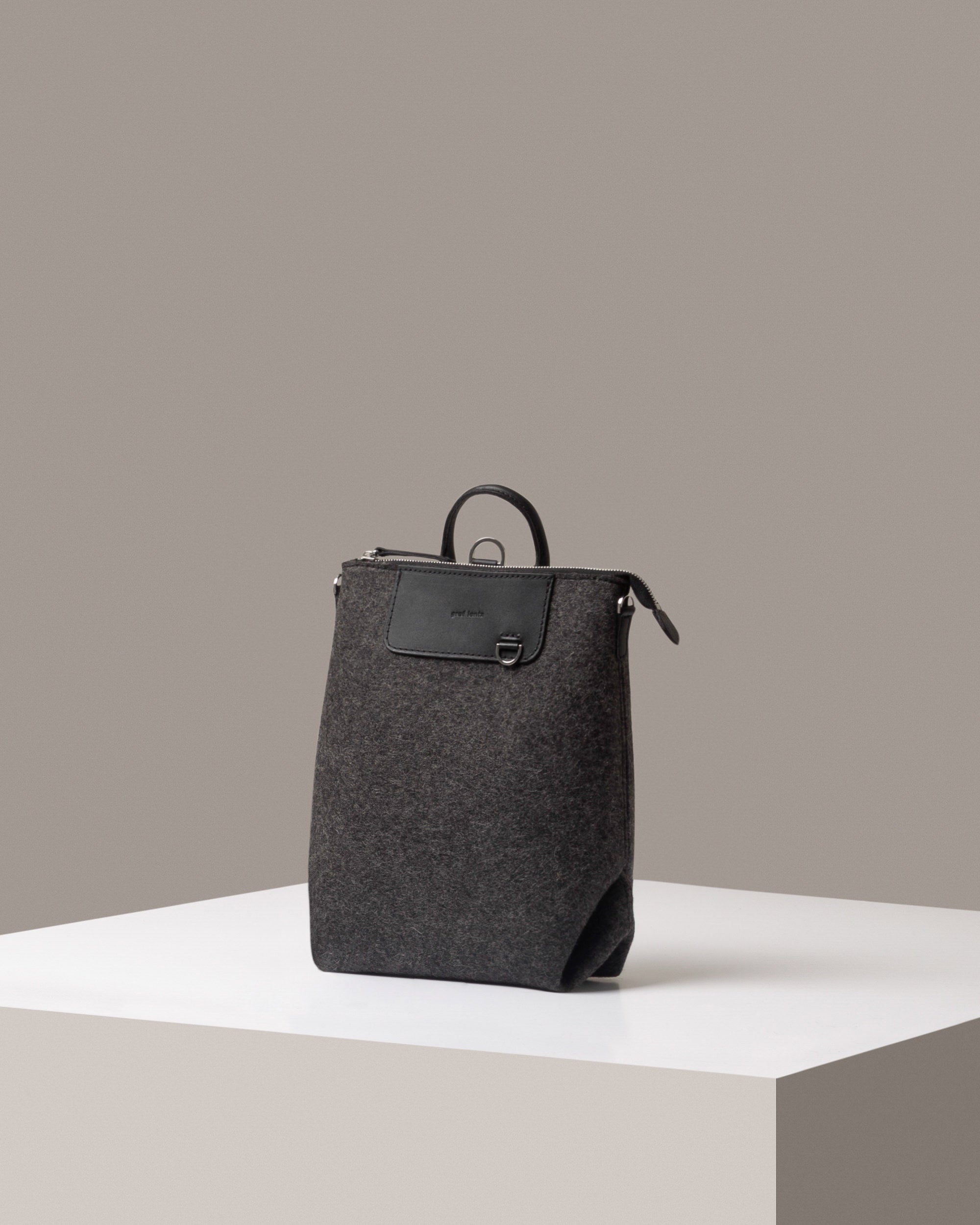 A Bedford Merino Wool Felt Midi Backpack in dark gray, displayed in a three-quarter view on a white base