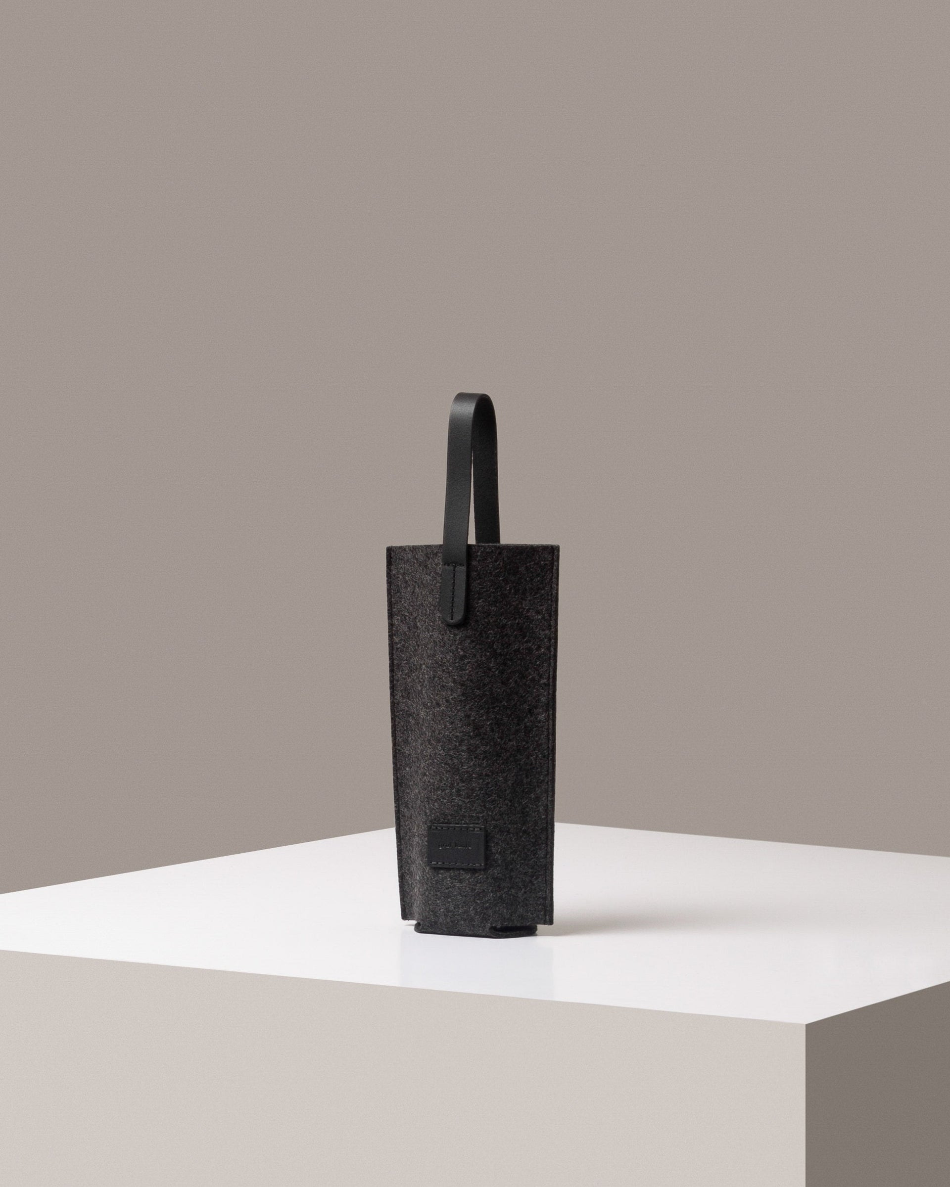 A stylish Hana Merino Wool Bottle Bag in dark gray, displayed in a three-quarter view on a white base