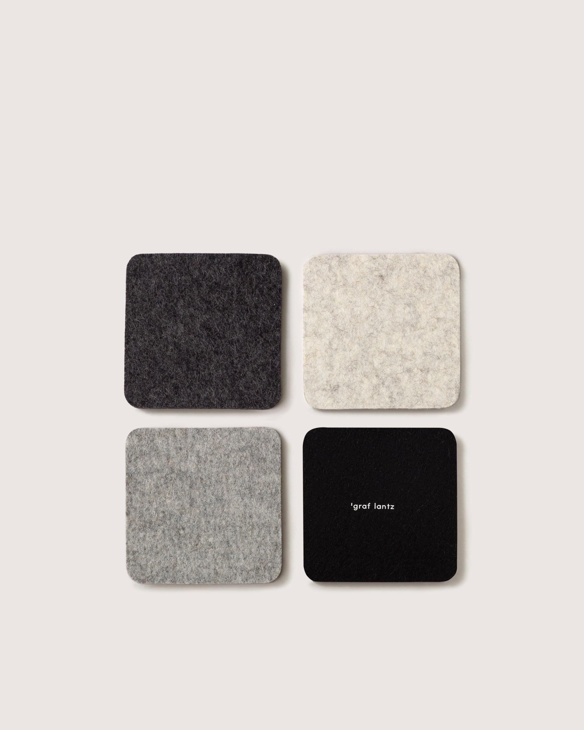 A 2x2 grid displays four square coasters made from German Merino wool in gray and black shades on a light background. The bottom right coaster features graf lantz in small white text, evoking the classic Bierfilzl style.