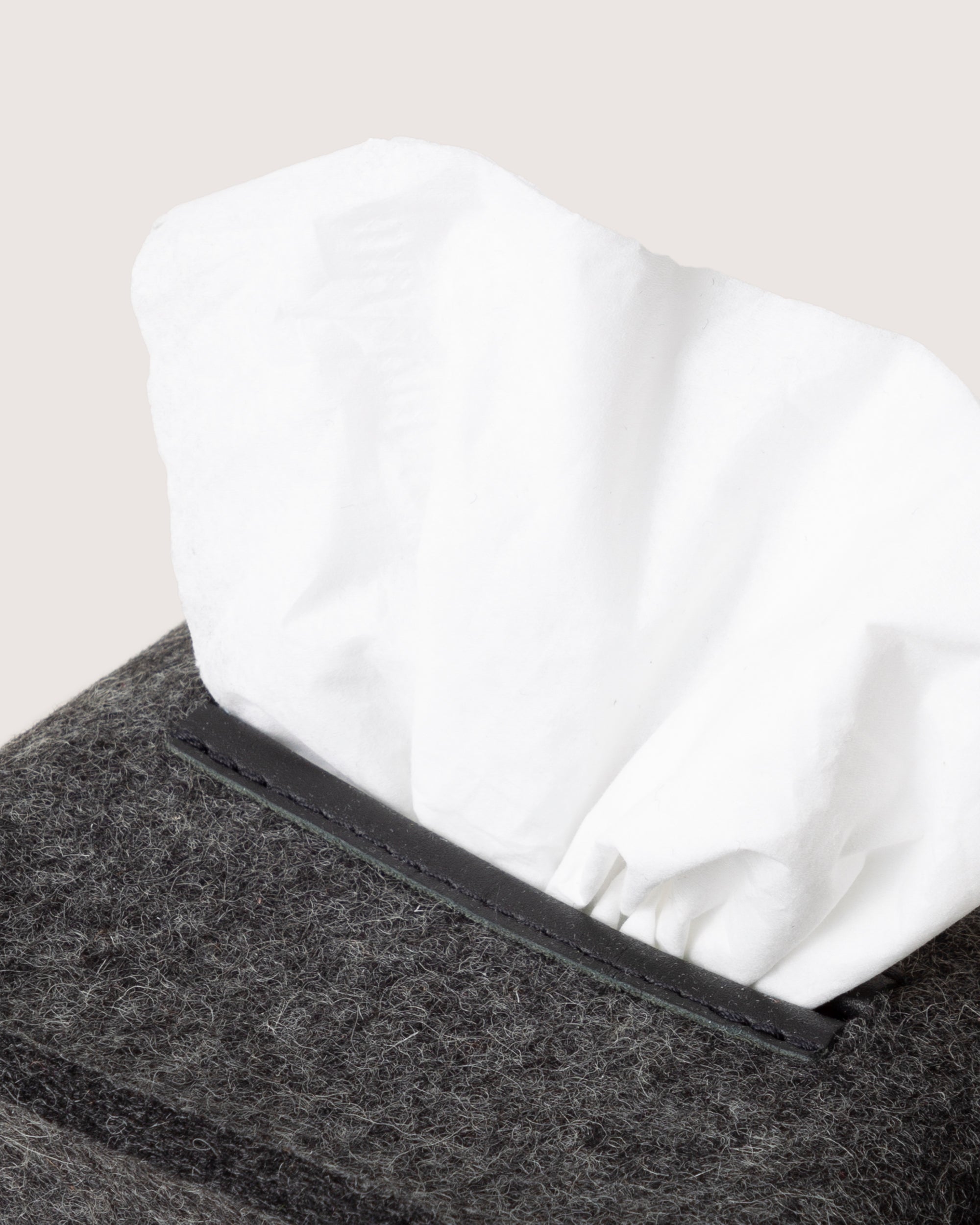 A white tissue peeks out from a textured, dark gray graf lantz tissue box on a light, neutral surface, elegantly enhancing your home décor.
