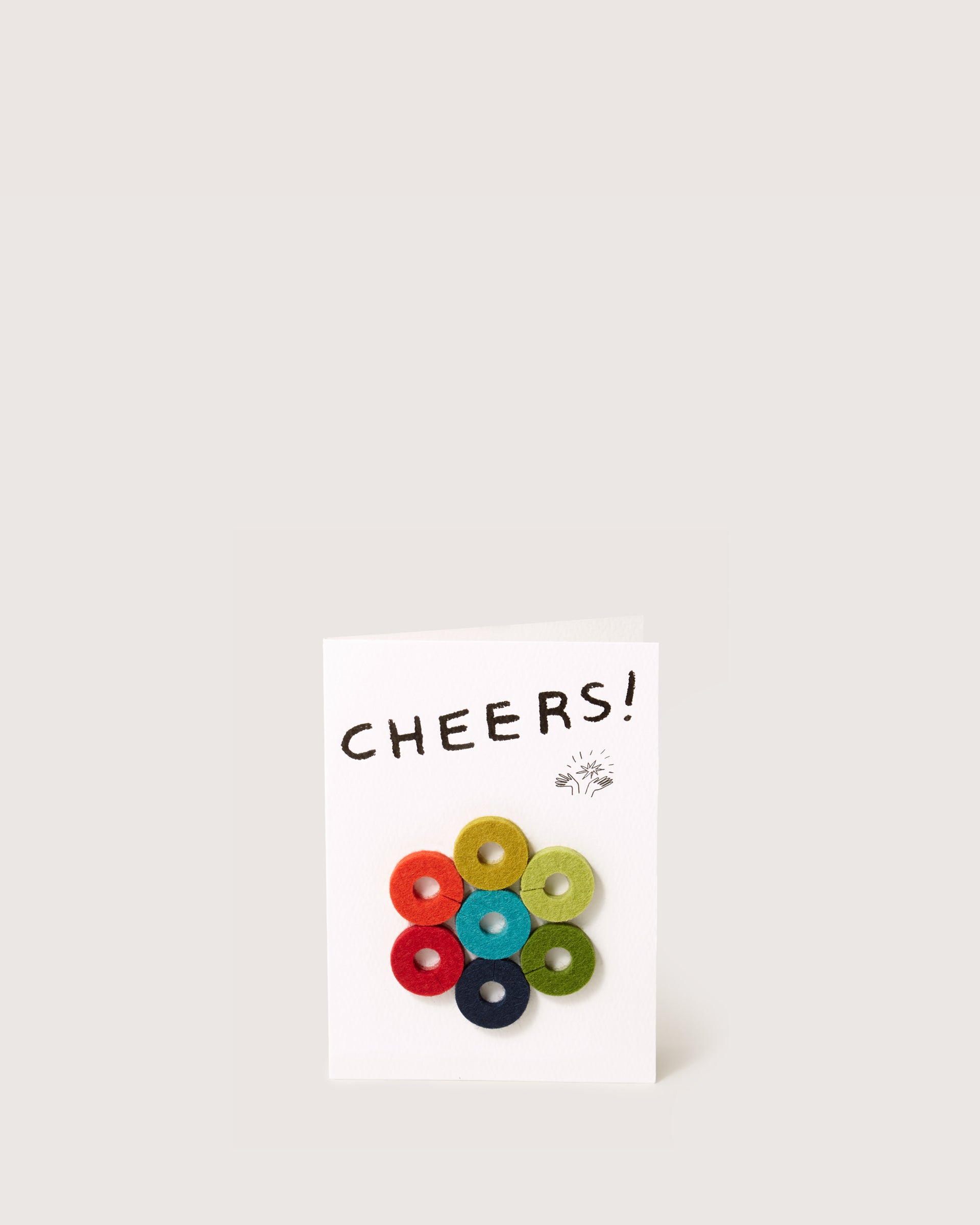 The graf lantz greeting card stands upright with CHEERS! at the top, showcasing seven colorful Merino wool felt circles in a floral design, making it an ideal host gift. It pops against its plain off-white background.