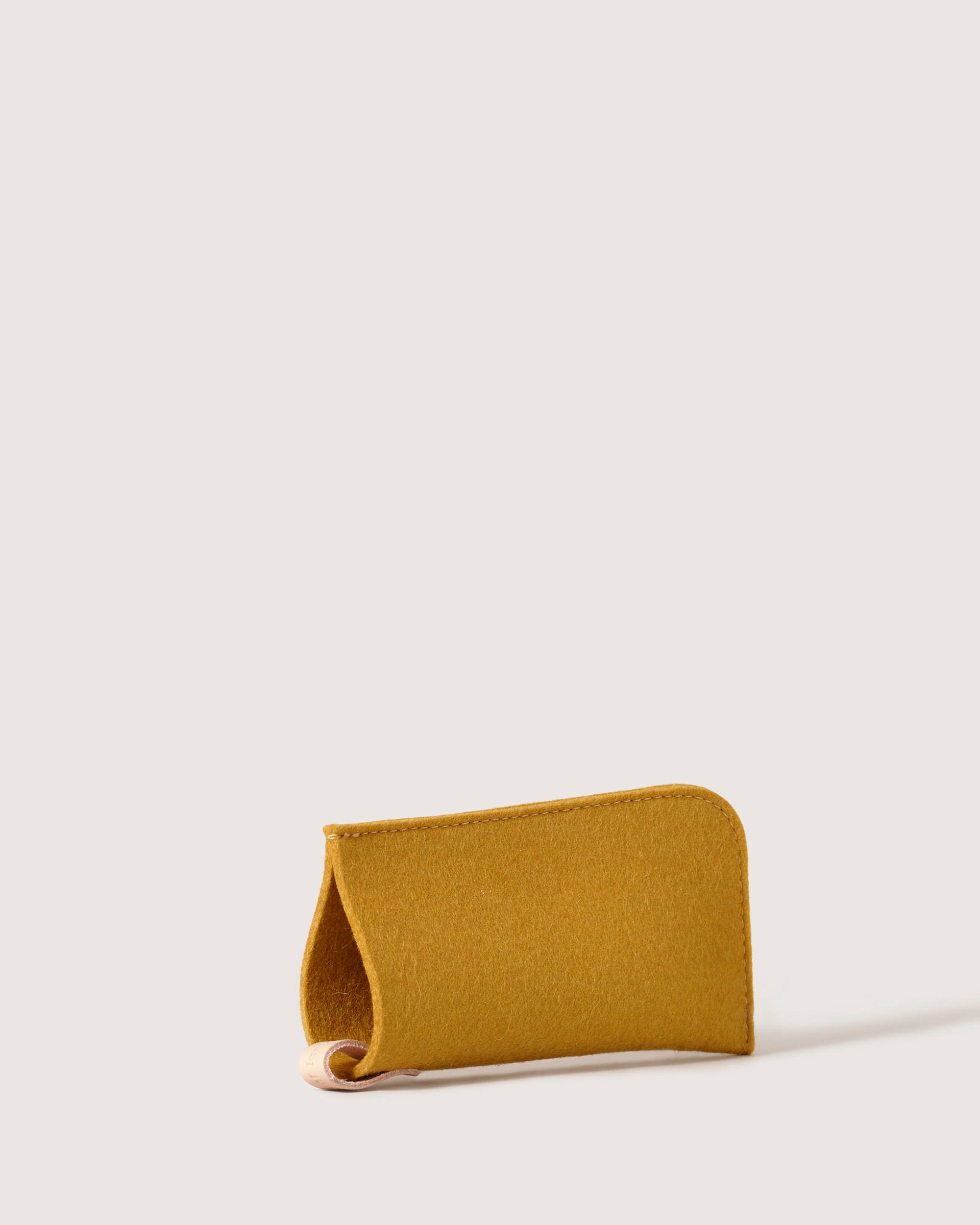 A mustard yellow Merino wool sunglass case by graf lantz with curved edges is centered on a light beige background. The top flap is folded open, revealing its interior. This minimalistic, stylish eyeglass sleeve ensures superb eyewear protection.