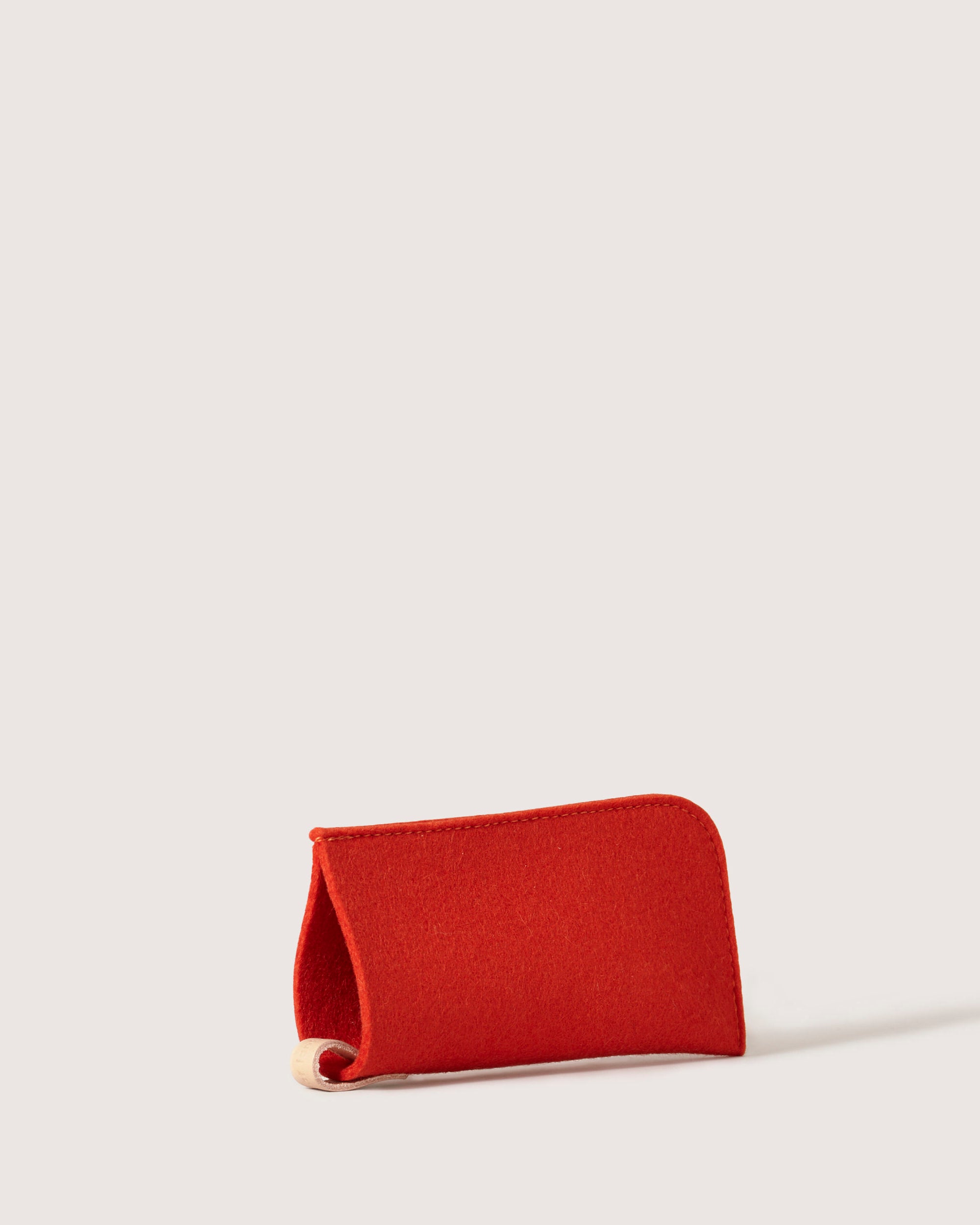 On a light background, the graf lantz red eyeglass sleeve stands upright, crafted from felt with a semi-circular opening and textured elegance. It offers premium eyewear protection in a simple, stylish design reminiscent of soft Merino wool.