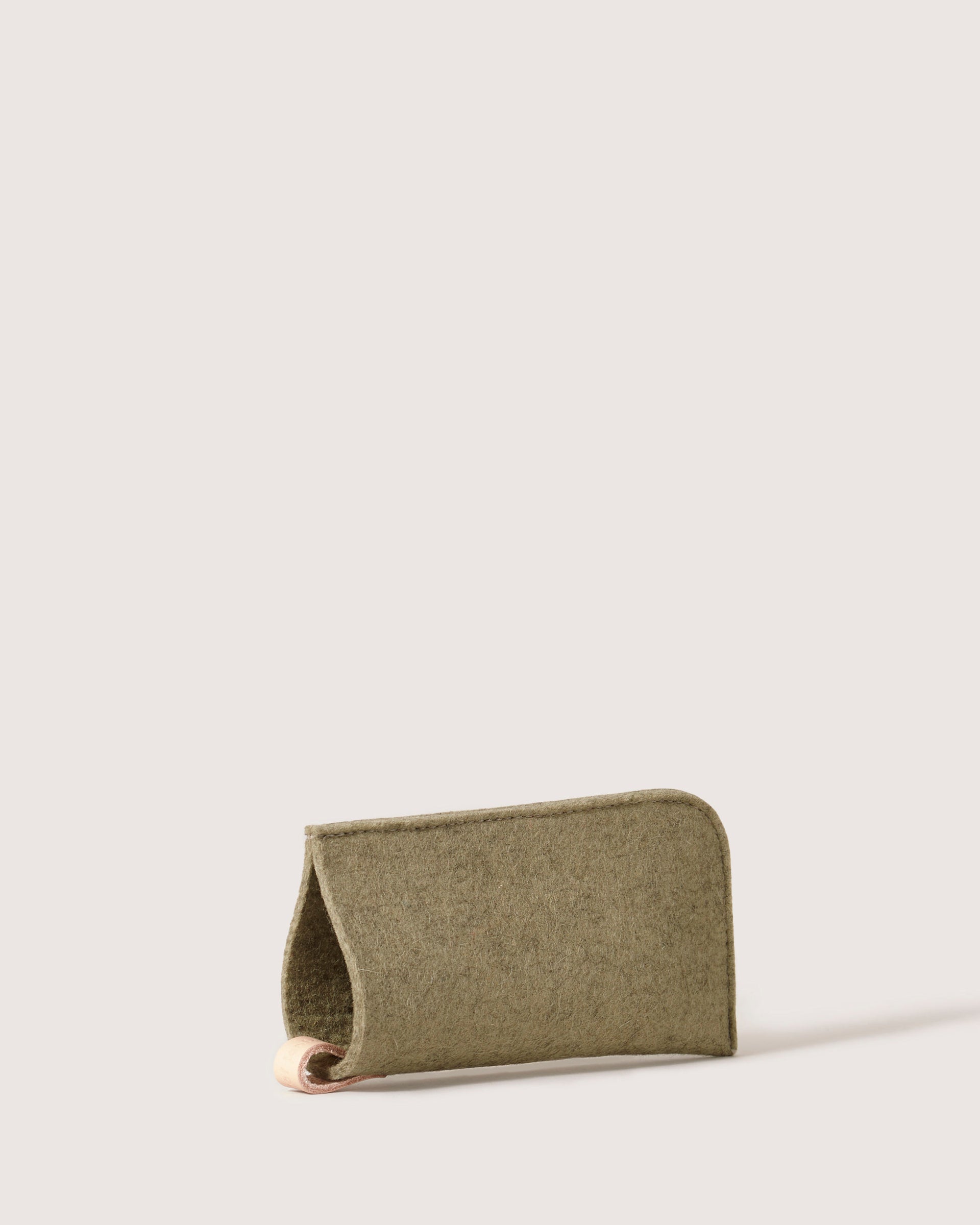 The graf lantz green felt eyeglass sleeve, made from Merino wool, features a minimalist fold-over design. Its soft texture offers eyewear protection and style, standing upright against a light background.