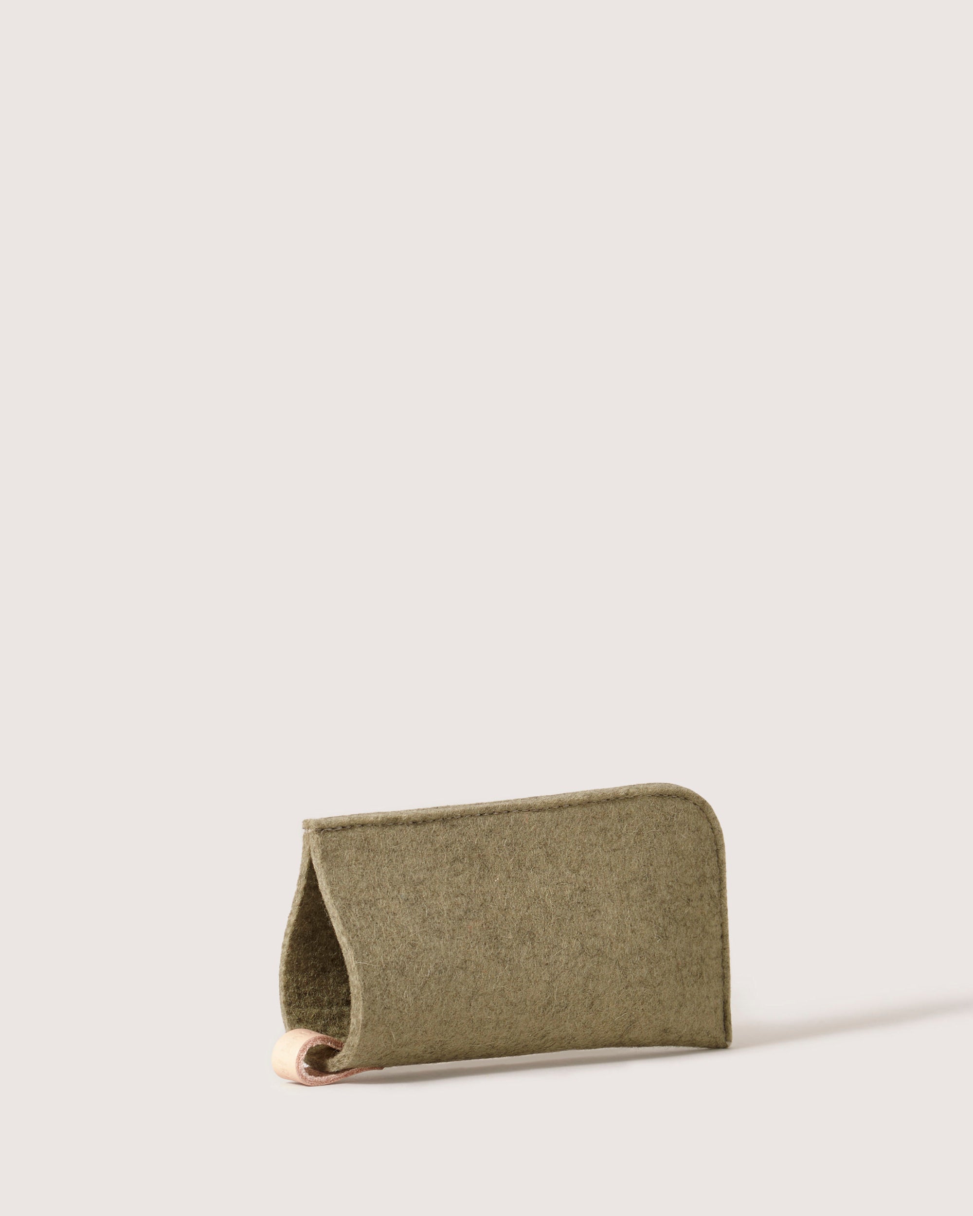 The graf lantz green felt eyeglass sleeve, made from Merino wool, features a minimalist fold-over design. Its soft texture offers eyewear protection and style, standing upright against a light background.