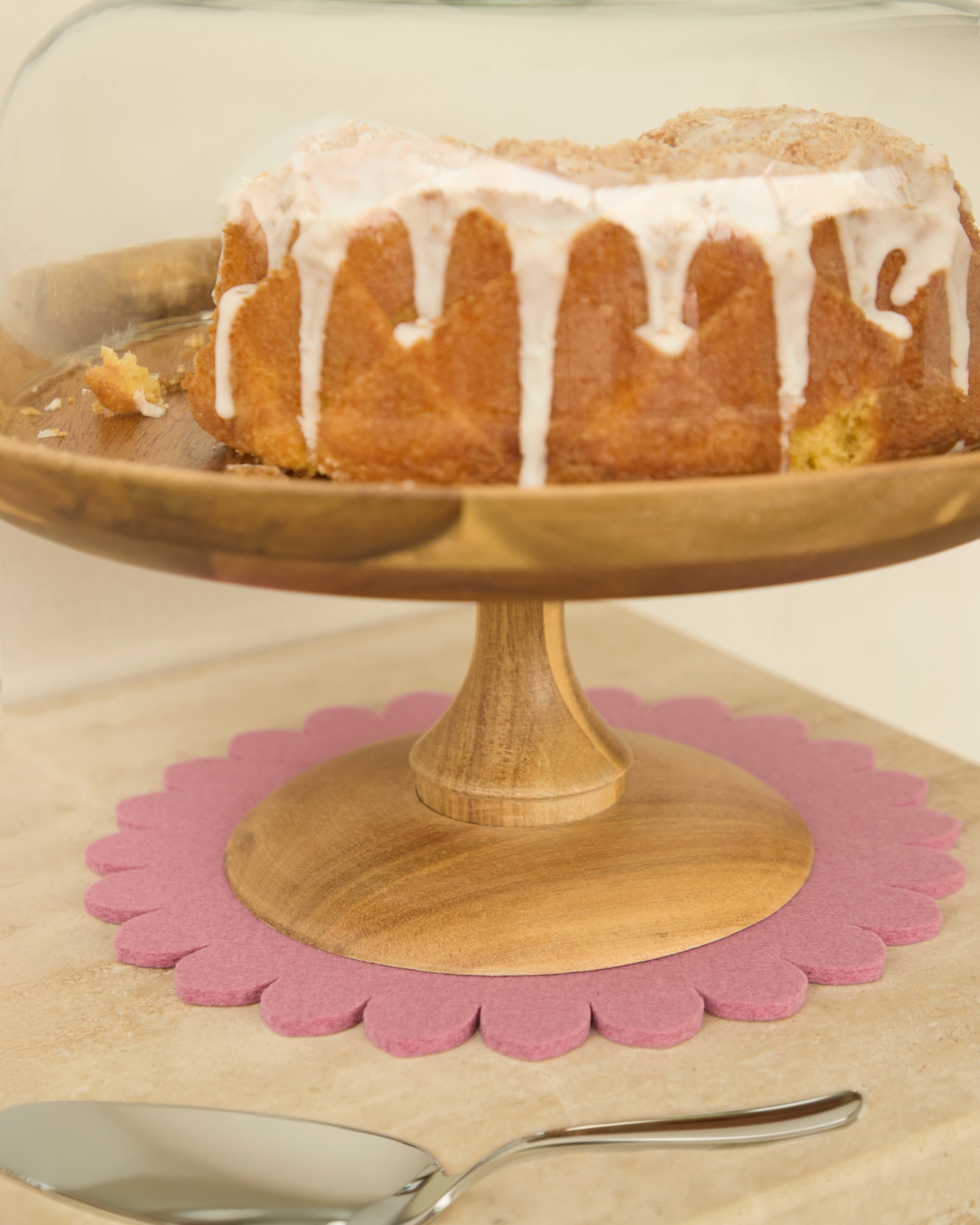 Cake on a wooden stand with a pink floral-shaped Merino wool trivet underneath