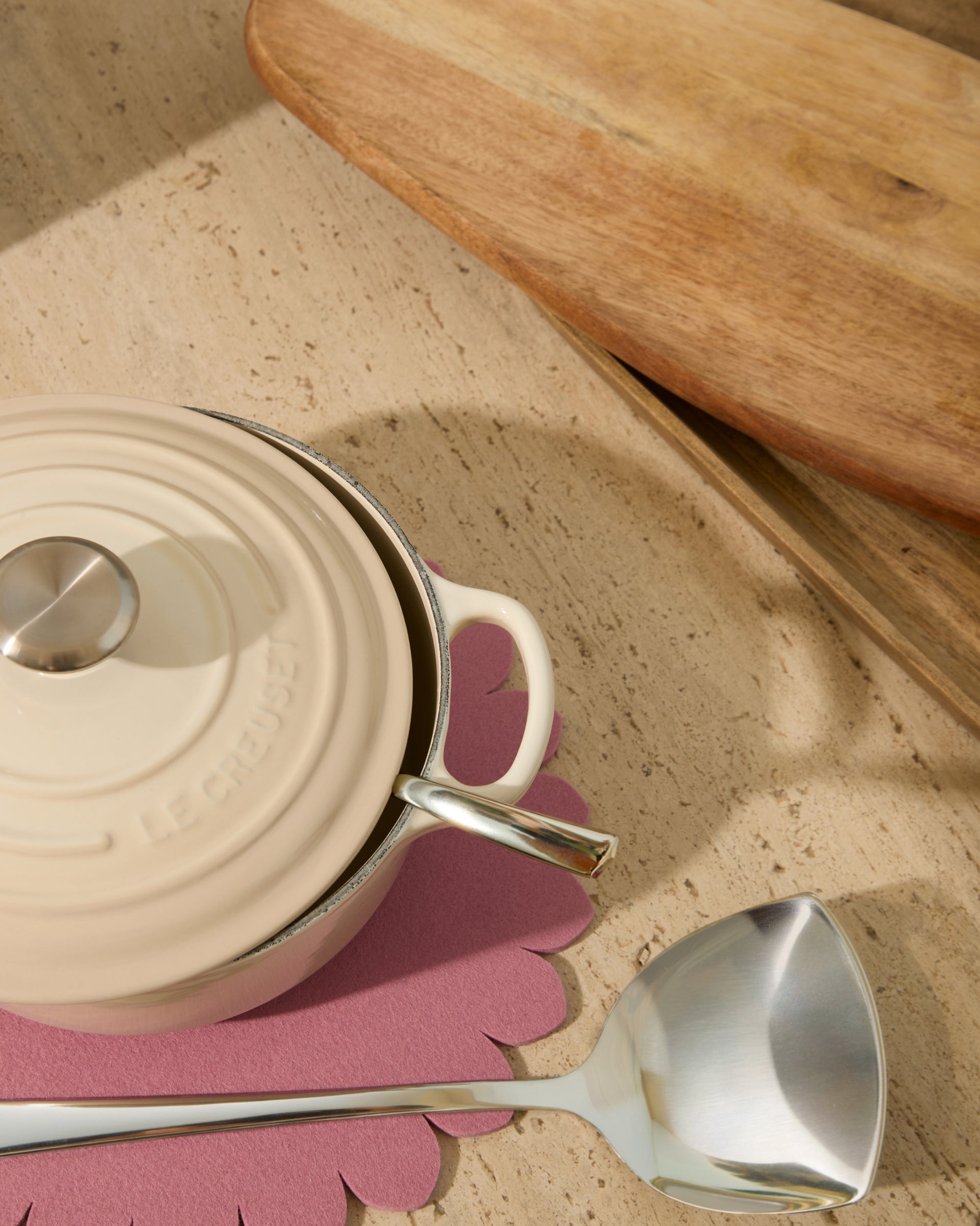 Cream-colored pot with a metal ladle on a mauve floral-shaped trivet.
