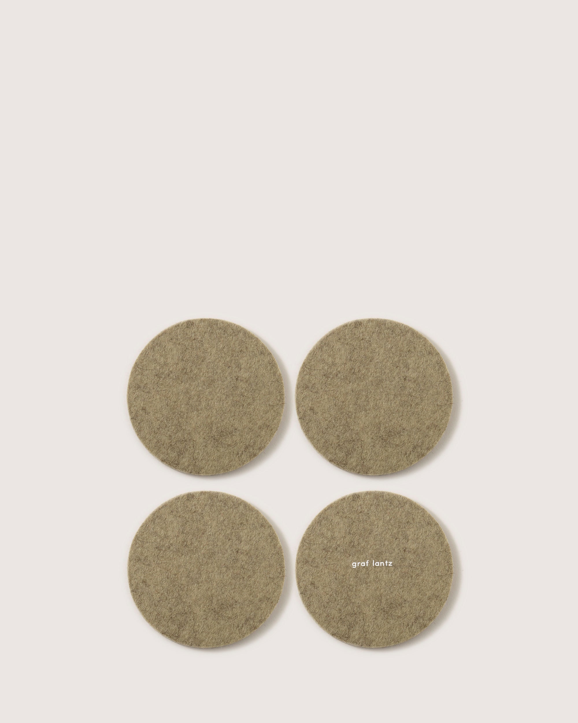 Four round, beige felt coasters made from Oeko-Tex Certified German Merino wool are arranged in a square on a plain background. One coaster showcases the graf lantz logo.