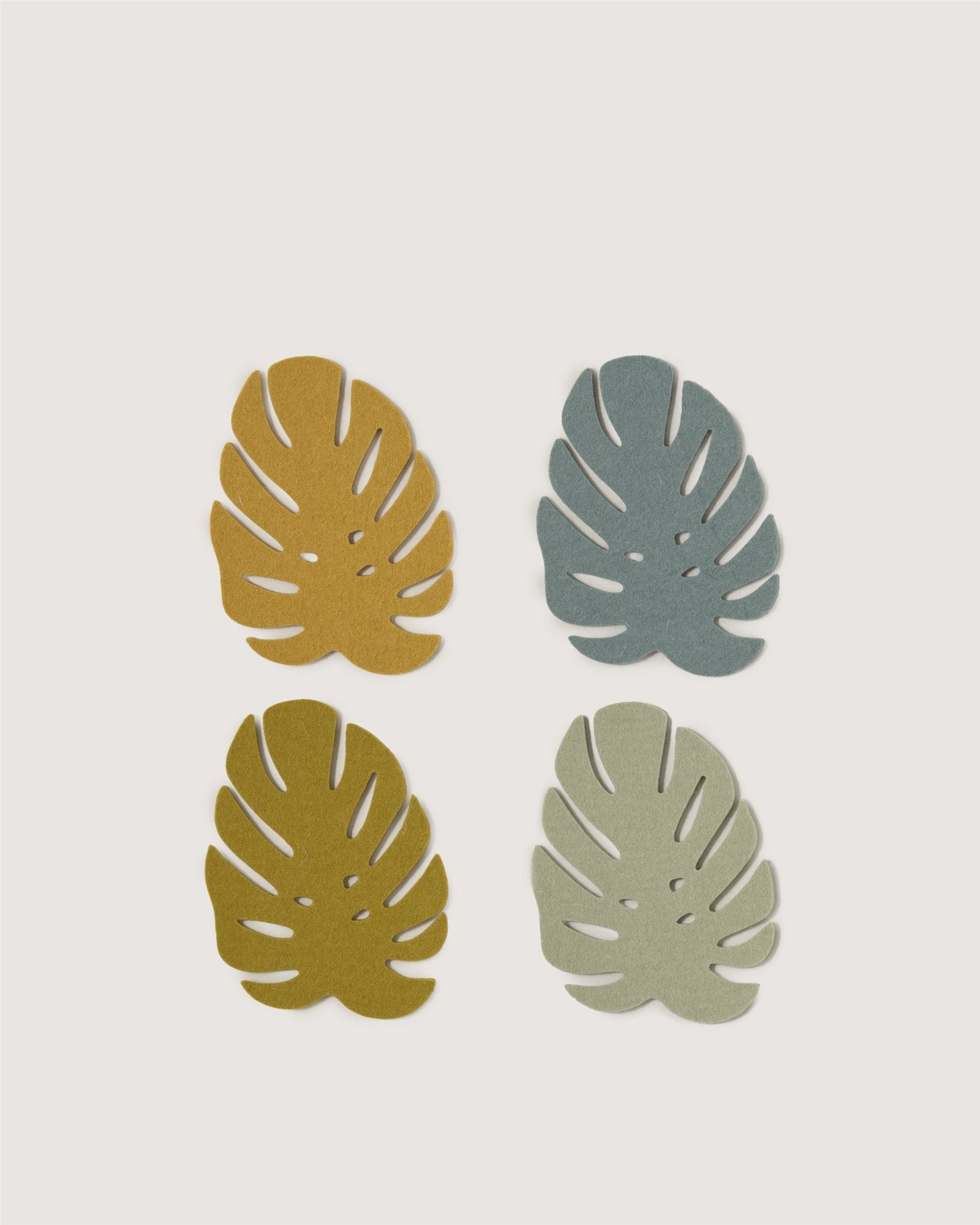 Graf Lantz’s four Merino wool Monstera coasters—in mustard yellow, teal blue, olive green, and light gray—are arranged in a 2x2 grid on a white background, perfect for adding sustainable style to your home decor.