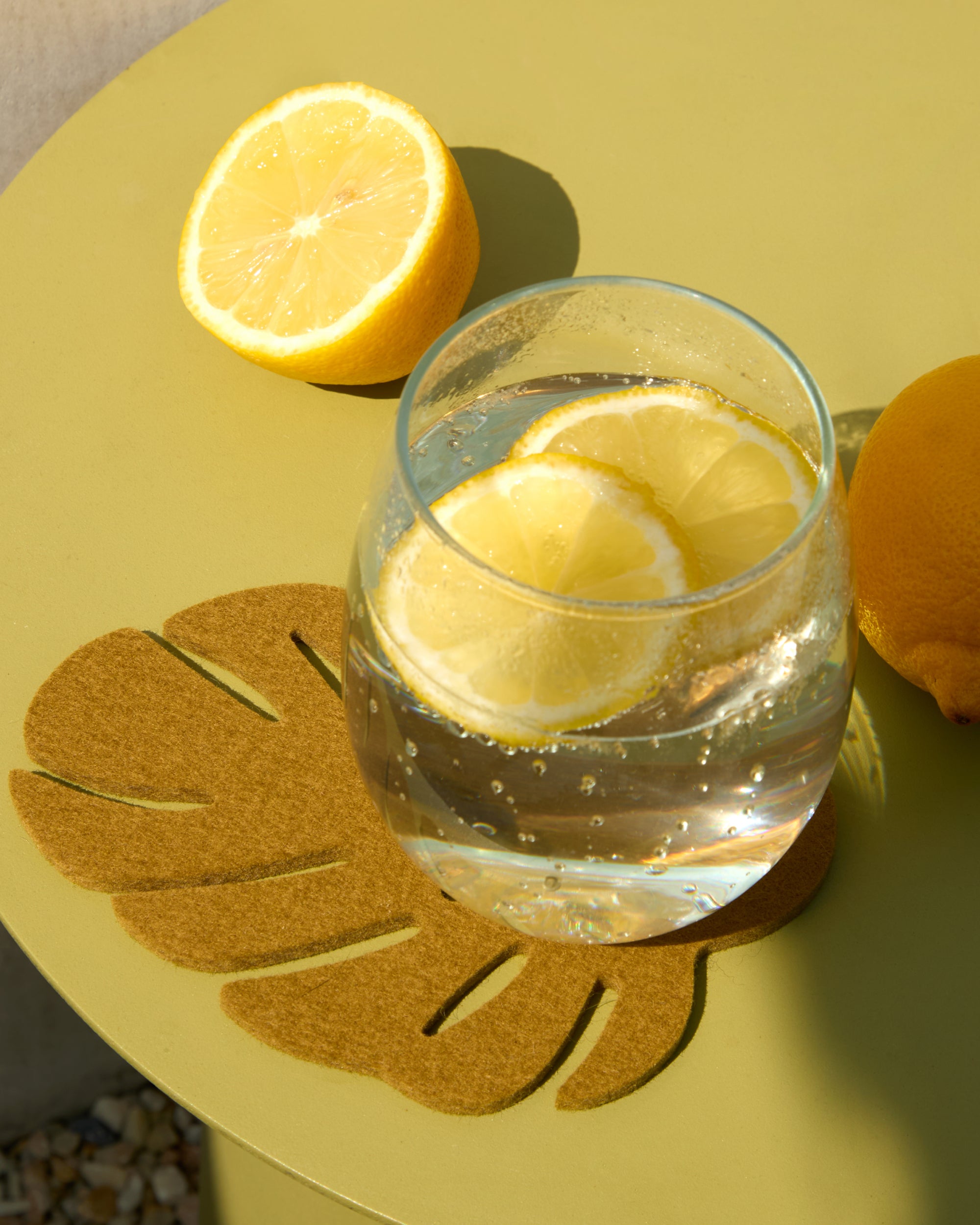 Glass of water with lemon slices on a yellow surface with a halved lemon and orange.