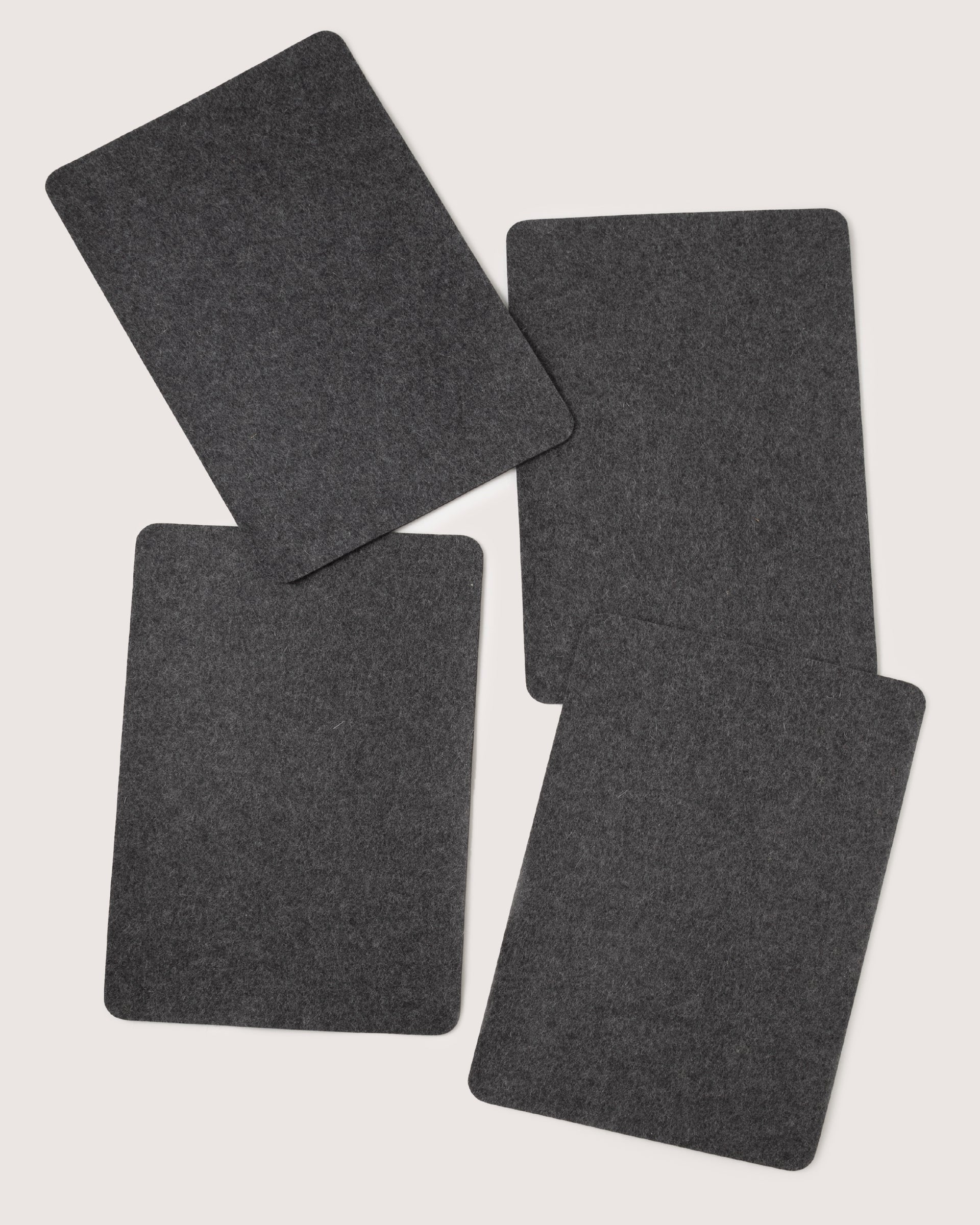 Four dark gray rectangular felt pads by graf lantz, made from premium Merino wool, are arranged in a loose, overlapping pattern on a plain white background for a designer-inspired look.