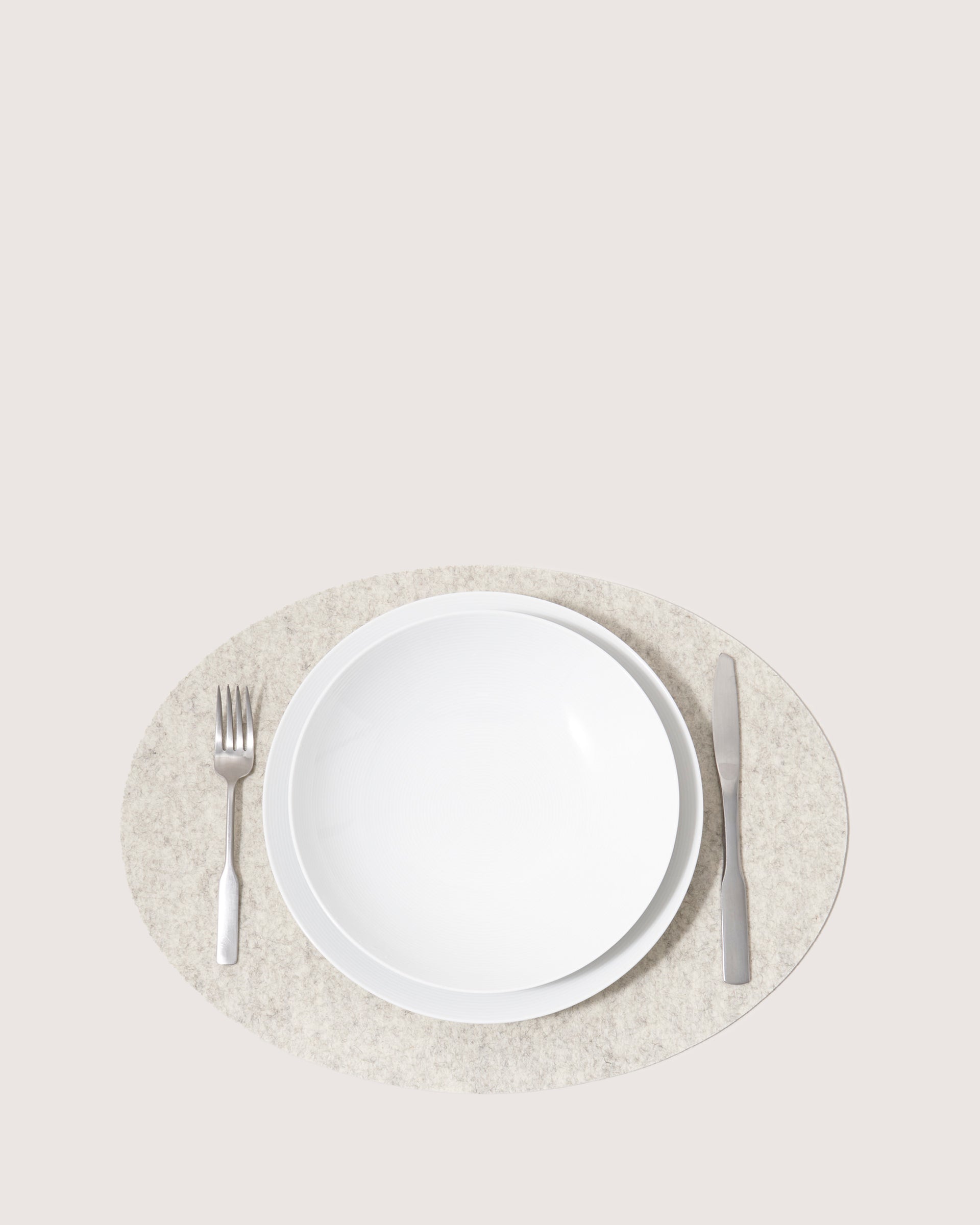 A white plate sits on a sophisticated graf lantz Merino Wool Placemat in light gray. To the left lies a stainless steel fork, and to the right, a knife. The light beige background accentuates this moisture-wicking and heat-resistant setups elegant allure.