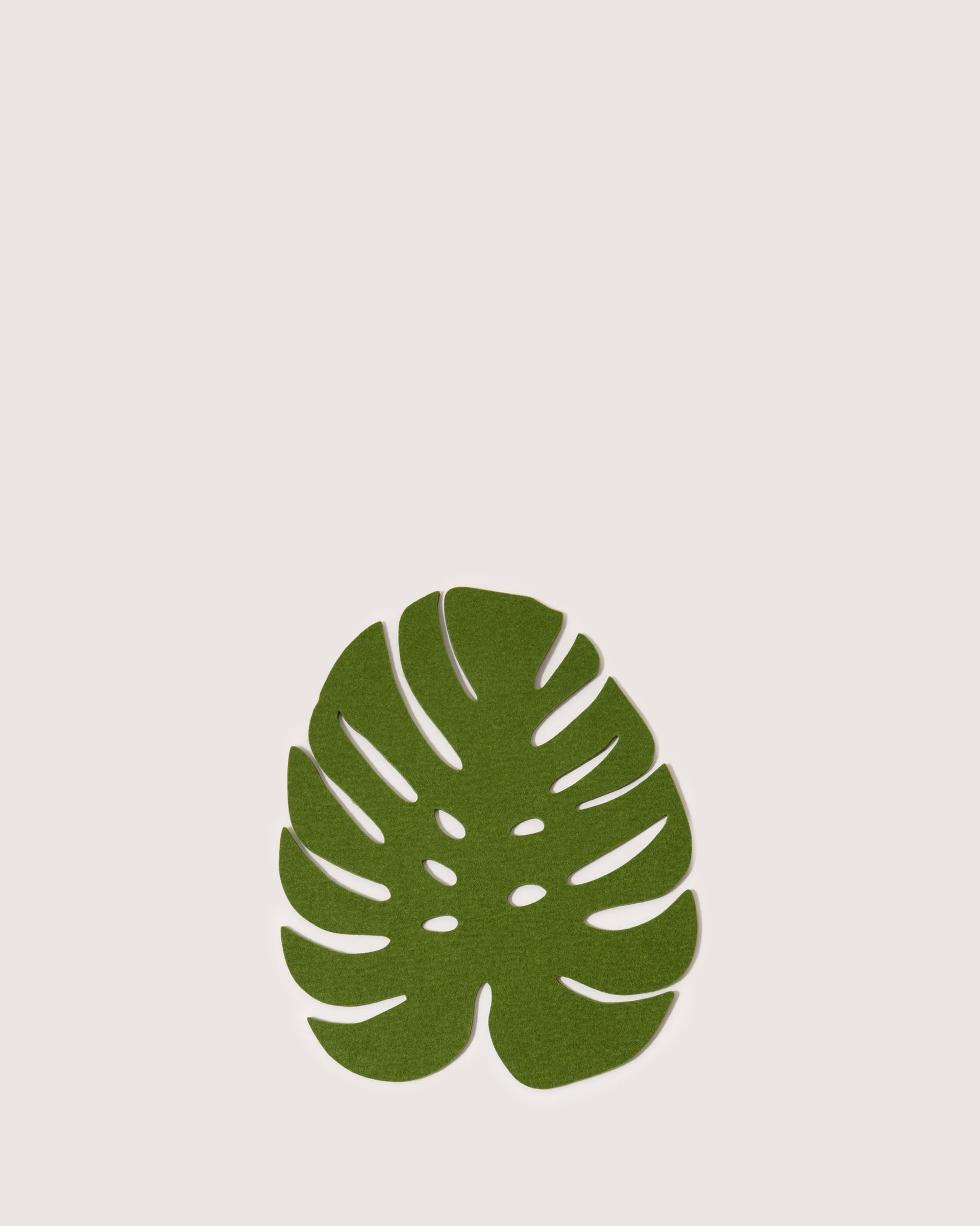 A sustainable green monstera leaf by graf lantz, featuring stylized cutouts and a smooth finish, rests against a plain white background like a decorative art piece.