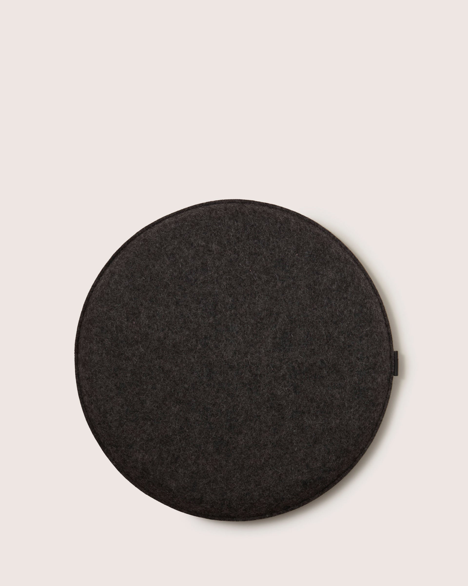 The graf lantz round Zabuton seat cushion in dark gray felt is made from soft Merino wool. It features a minimalist design, making it ideal for meditation or relaxation, and it rests against an off-white background.
