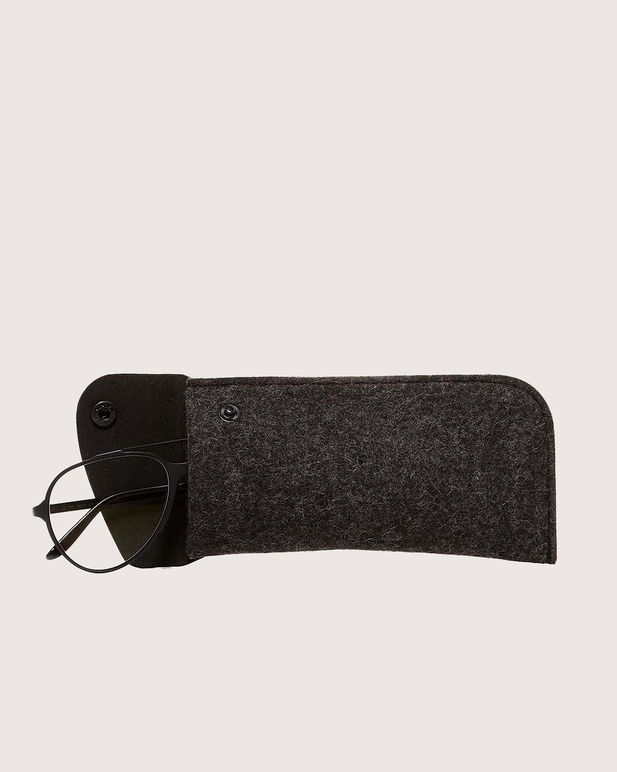 A pair of black eyeglasses is partially pulled from a dark gray felt case with button closure by graf lantz, made from Oeko-Tex® Certified Merino wool. The sleeve elegantly rests on a plain light background.