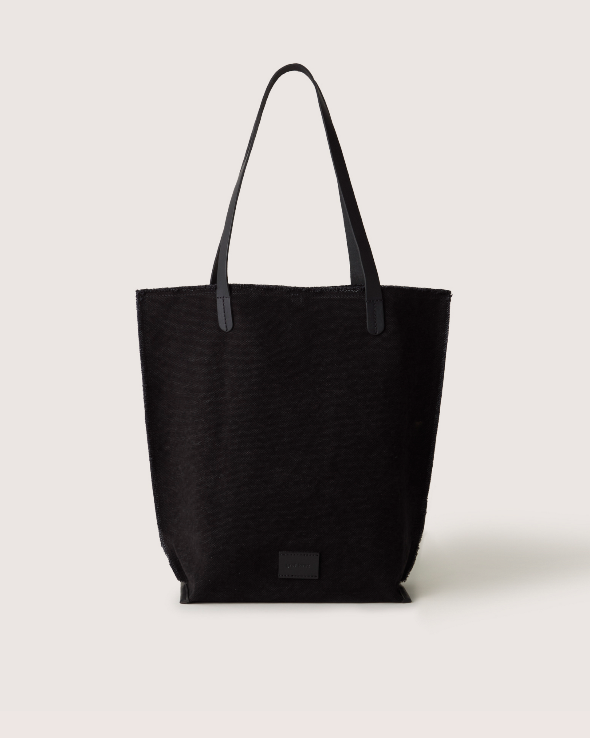 A black Graf Lantz canvas tote with structured leather handles sits on a light background, showcasing its textured durable cotton canvas and a subtle front patch.