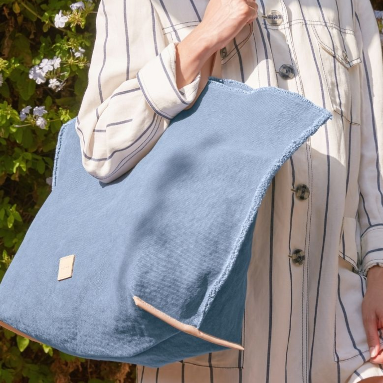 Person holding a Horizon-blue canvas bag outdoors with greenery in the background