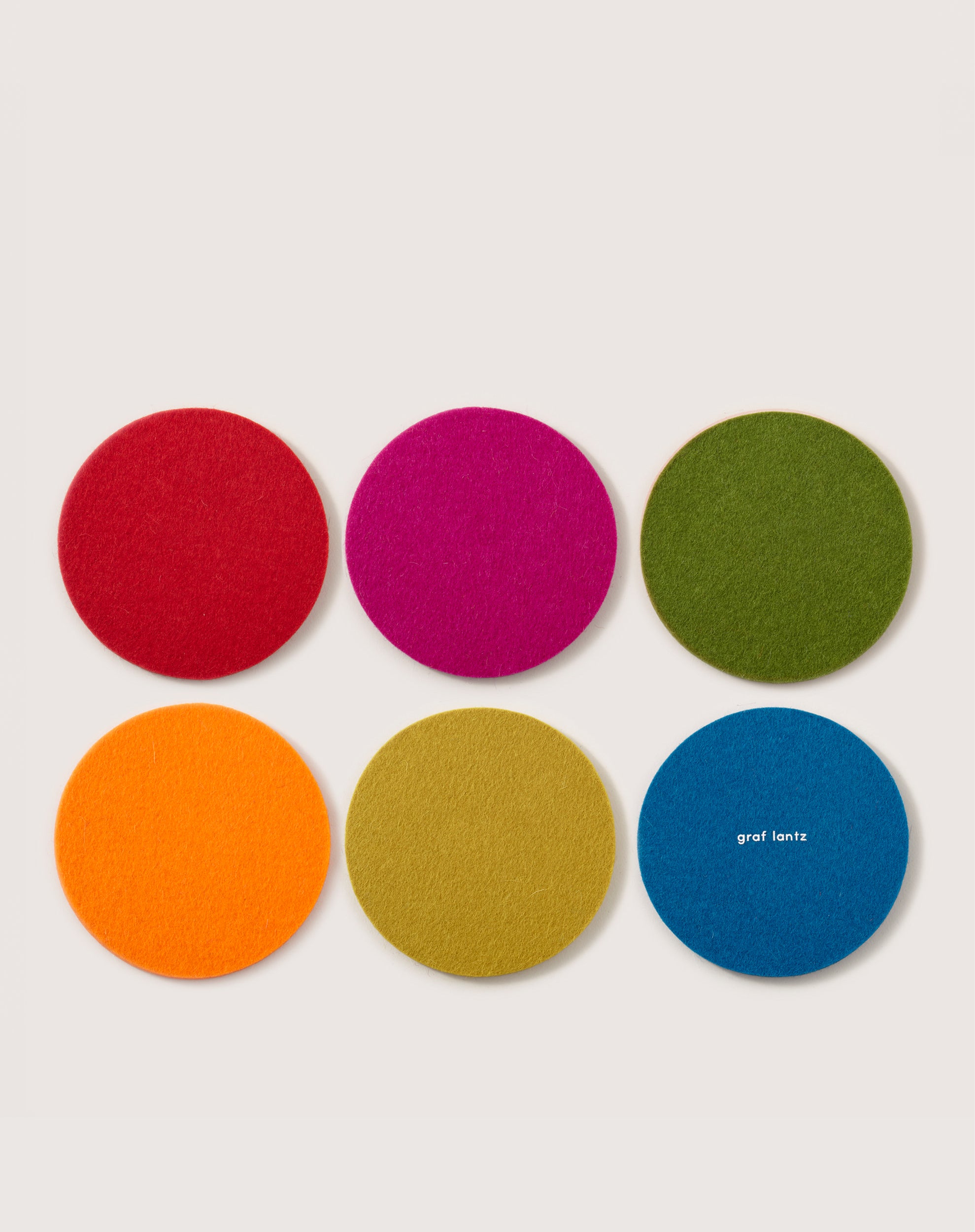 Six colorful Merino wool coasters by graf lantz are presented in two rows: red, pink, and green above orange, yellow-green, and blue. Crafted from sustainable materials, these pairs elegantly with a Kobon leather tray.
