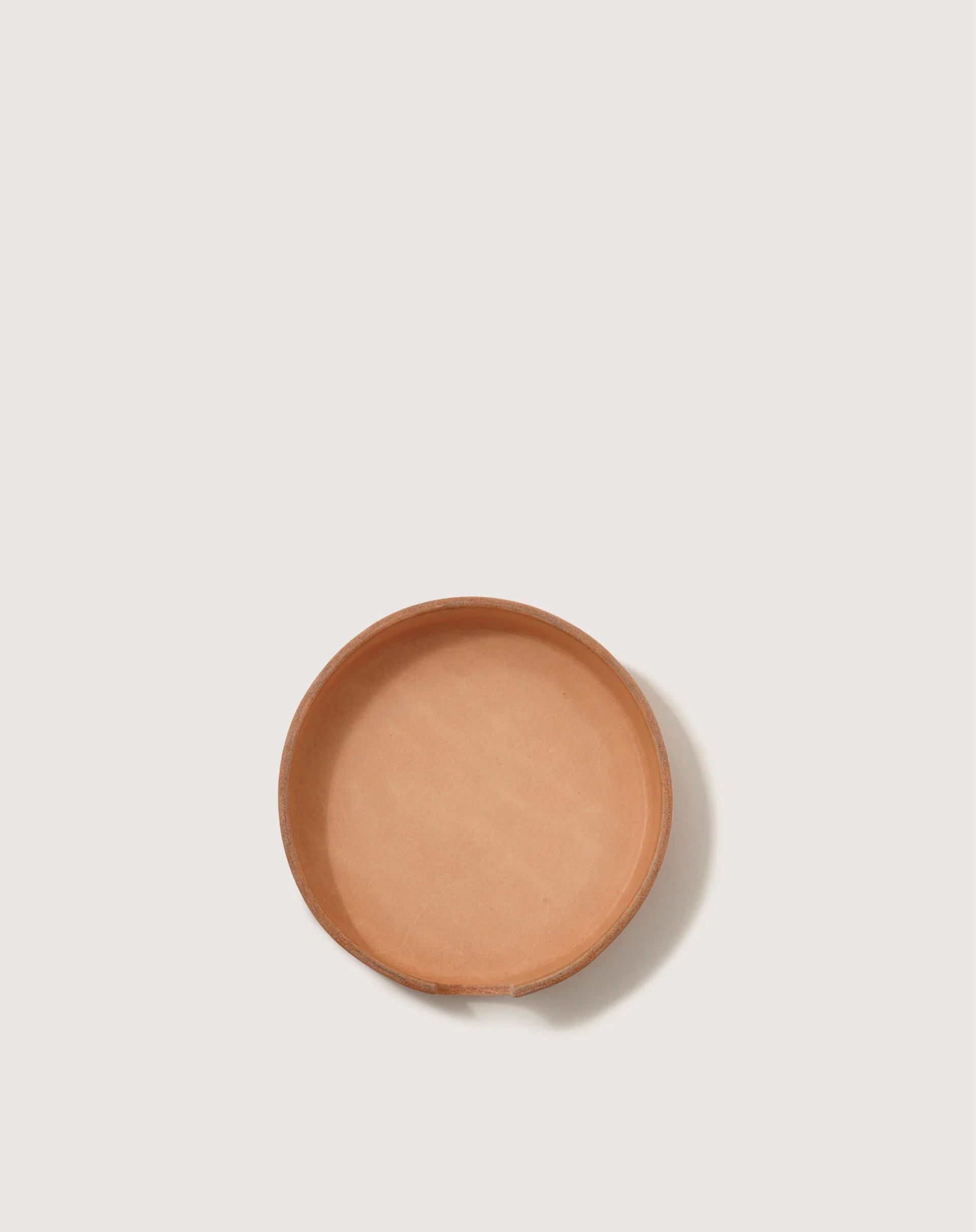 A round terracotta dish by graf lantz elegantly rests on a plain light backdrop, seen from above, resembling a versatile organizer for your cherished Kawabons.