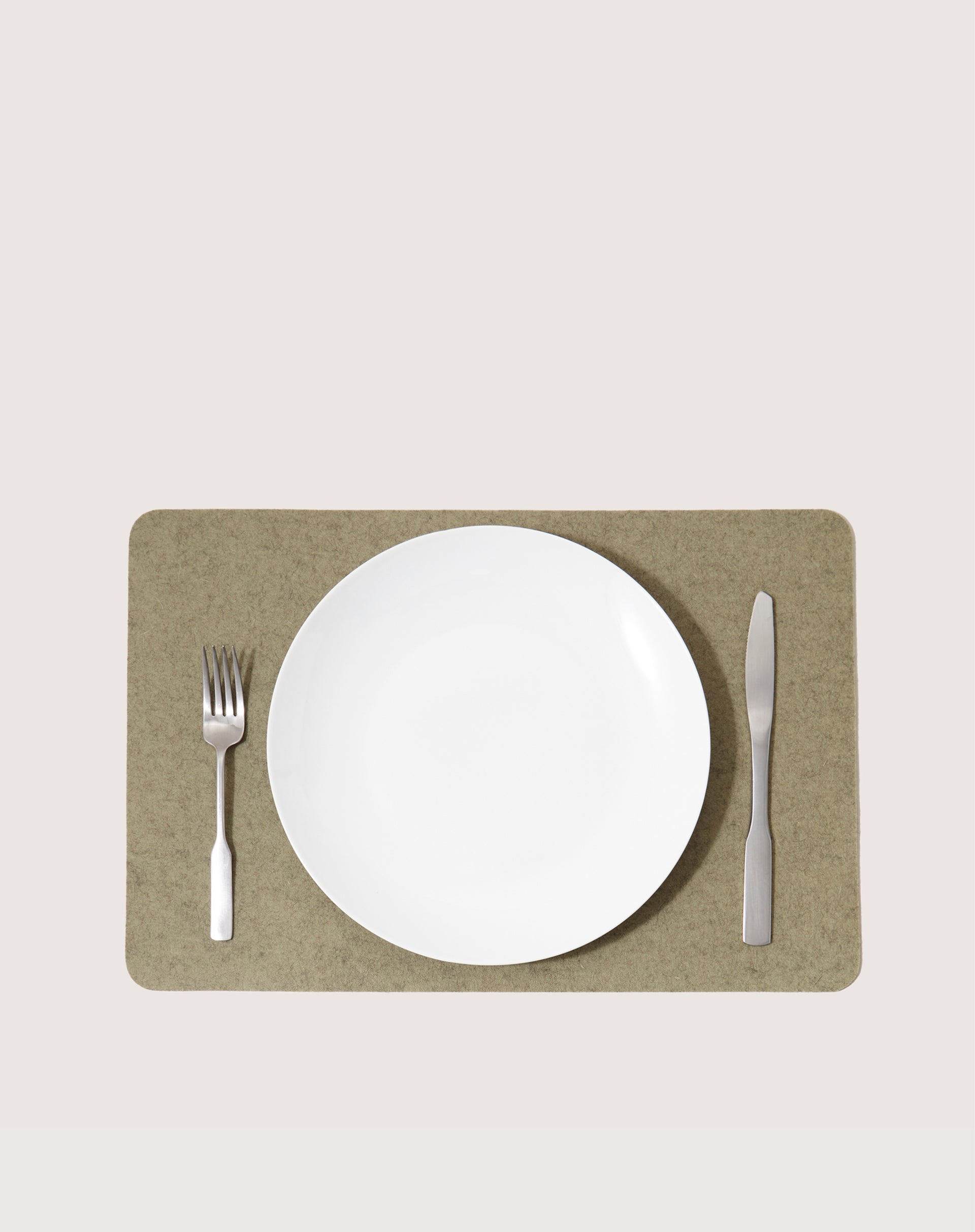 A white plate sits centered on a graf lantz rectangular Merino Wool Placemat. A fork lies to the left, and a knife to the right. The placemat, with its heat-resistant and moisture-wicking properties, adds elegance against the plain light background.