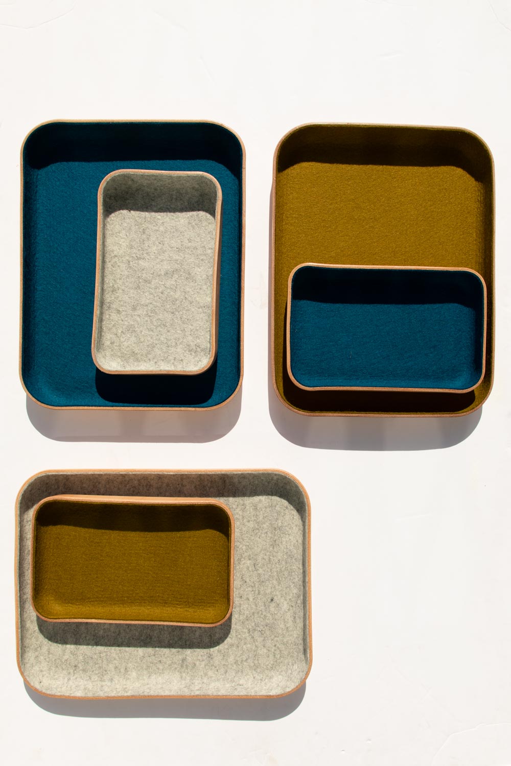 The graf lantz Kawabon catchall tray set includes four nested trays in square and rectangular shapes, lined with blue, mustard, and gray felt. Ideal for a housewarming gift, they are beautifully displayed on a plain white background.